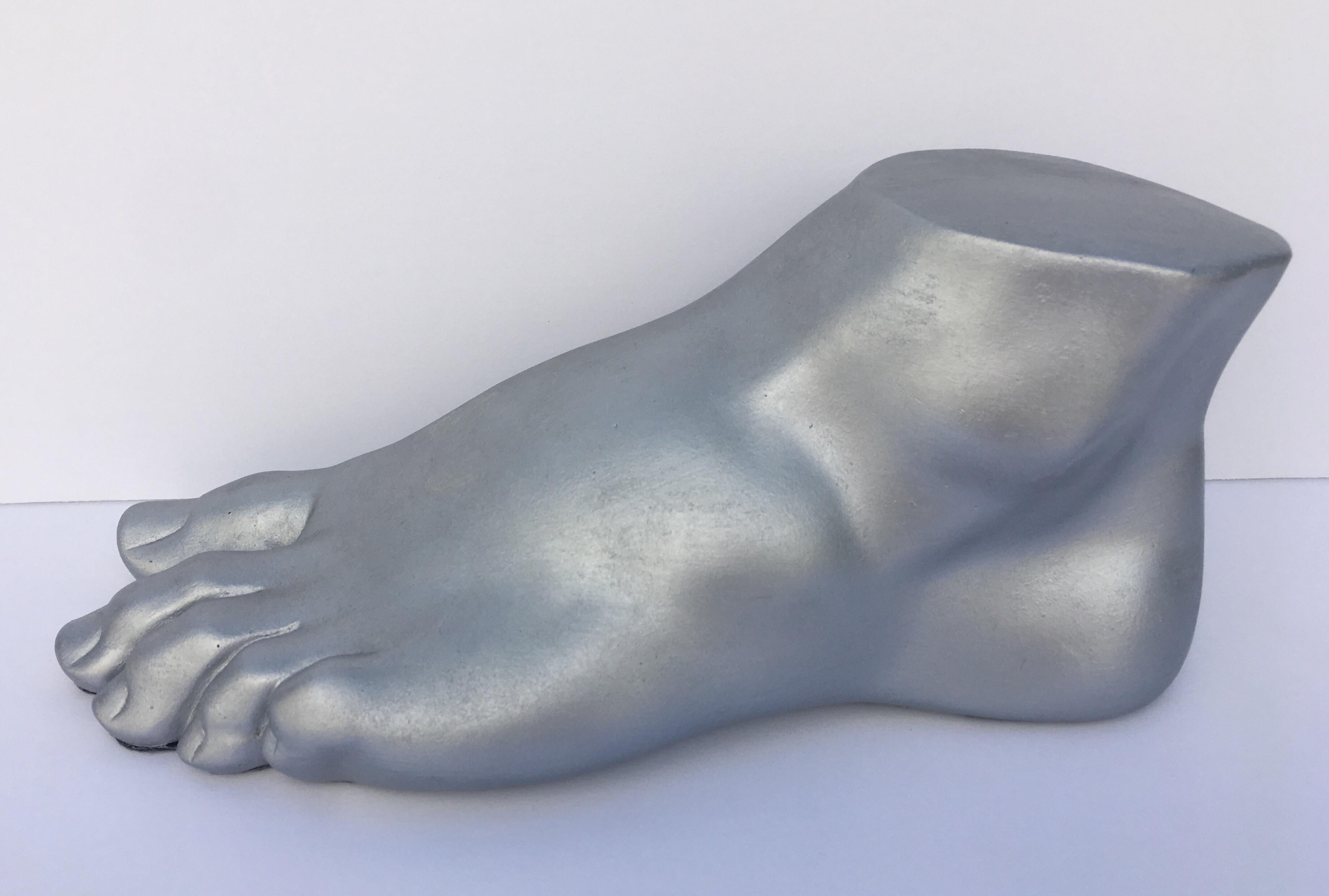 Neoclassical style plaster cast foot fragment sculpture featuring a patinated silver metallic finish. An interesting tabletop accessory for any Hollywood Regency interior.