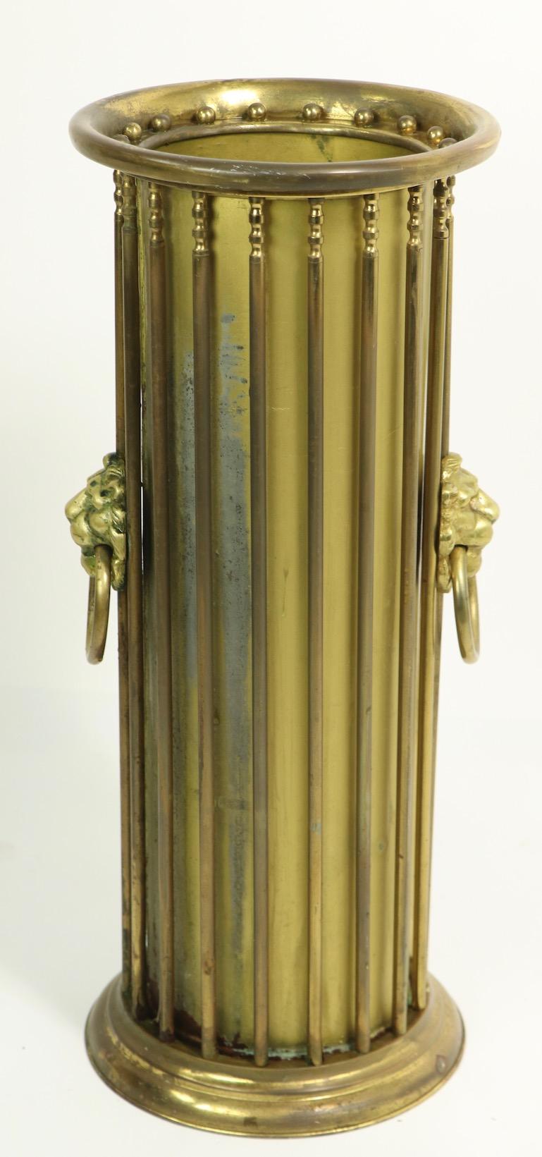 Classical Revival brass umbrella, or cane stand of cylindrical form with repeating brass rods and cast brass lions heads. Probably 1920s American made in the English style, this example does show some wear to finish and loss of brass tubing at the