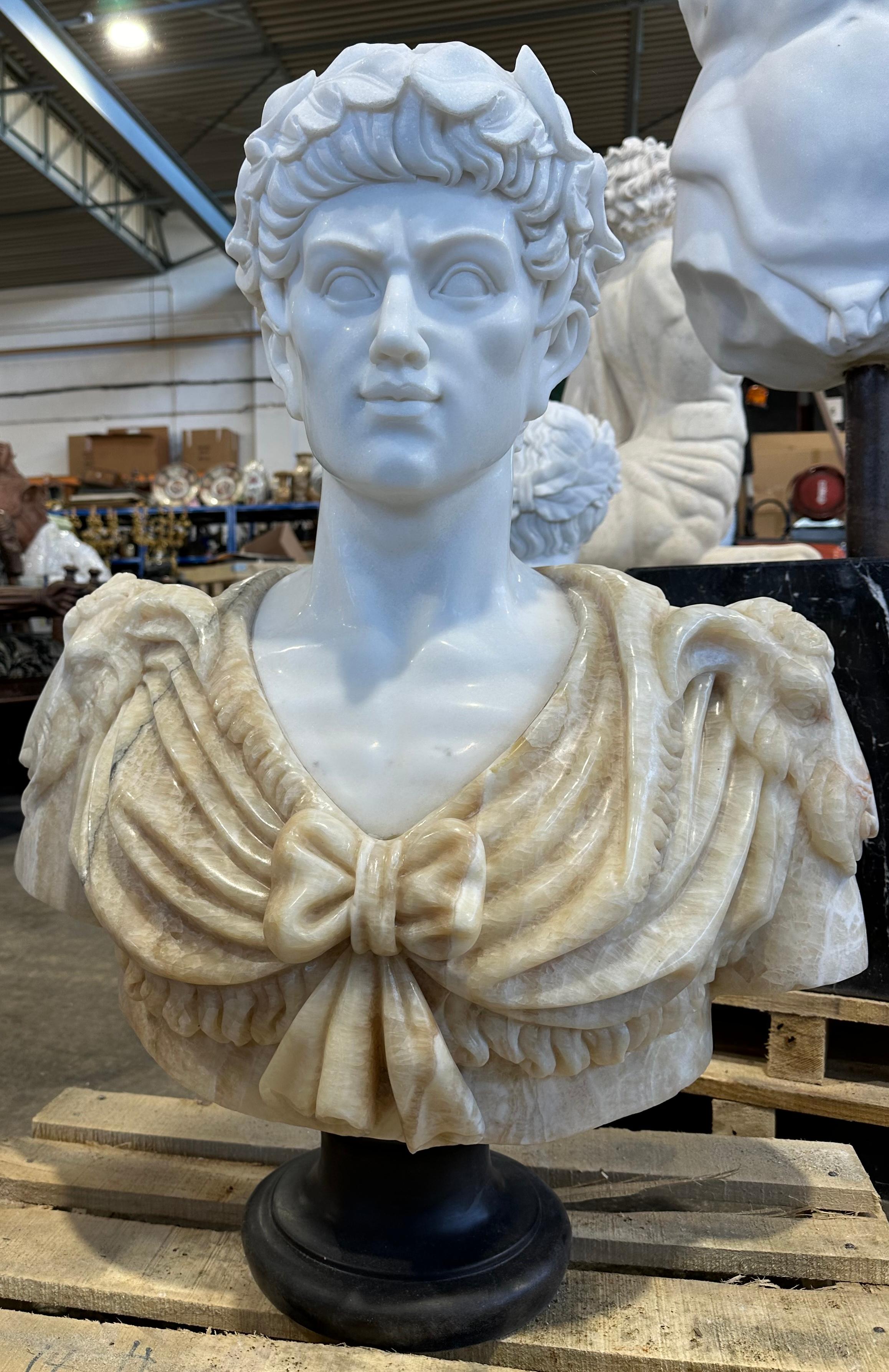 A decorative two coloured marble bust. Cleanly carved with delicate features, from the curling hair to the smooth draping of the cloth garments. Wearing a laurel wreath. An intricately carved rams head adorns each shoulder.  
This bust would look