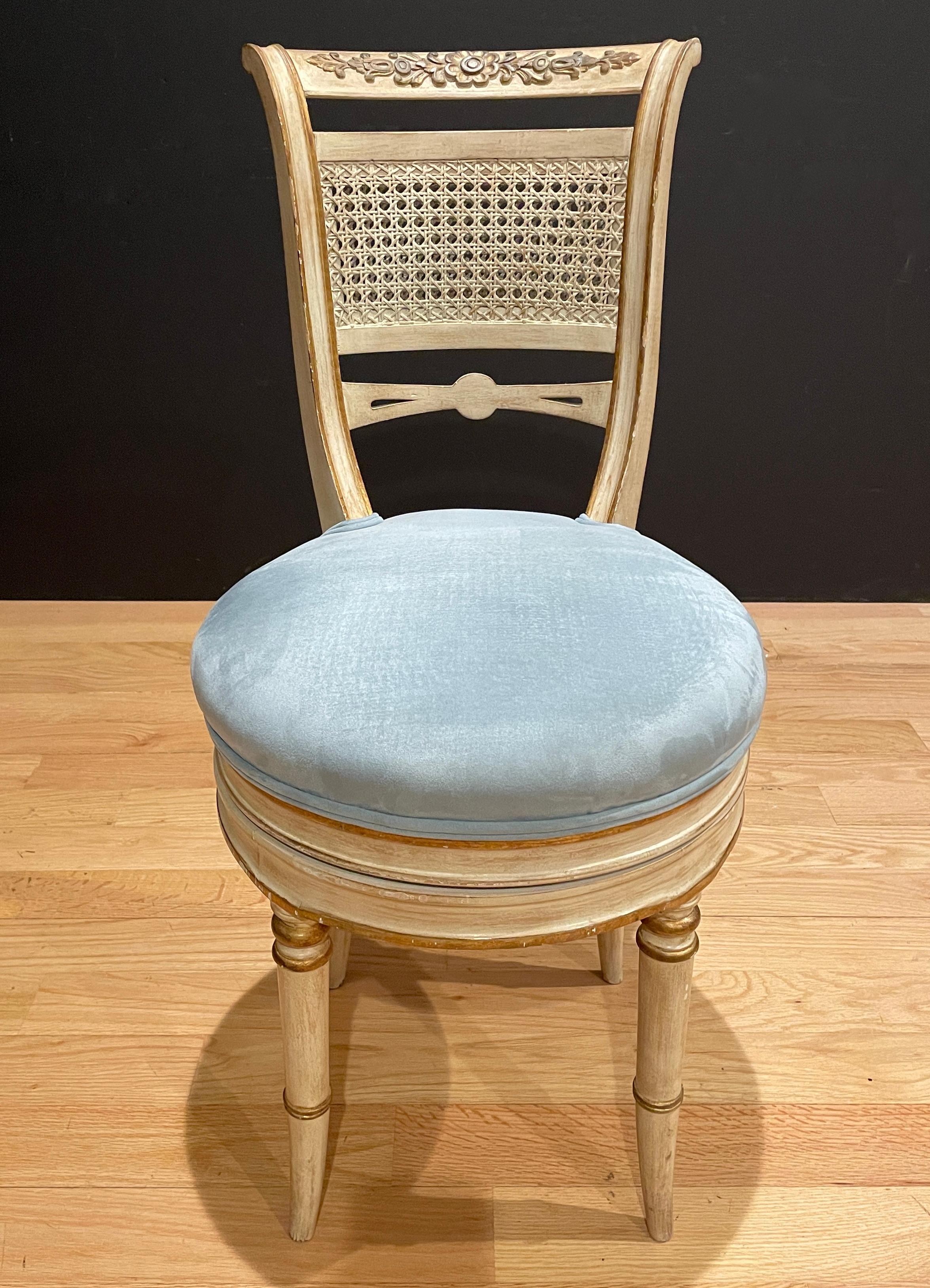 White painted and gilt classical design vanity/dressing/music chair. Blue velvet upholstery with hand carved and gilt details with double canning back. Chair swivels but does not adjust up.