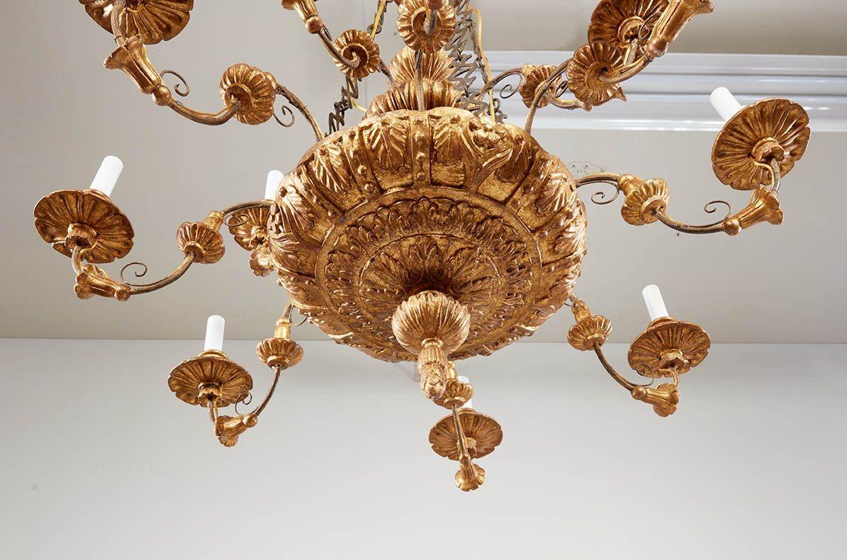 Un lampadario classico molto raffinato con una fila di quattro bracci sopra una fila di otto bracci di candelabri elettrificati, con un elaborato intaglio ad acanto che parte dalla corona in alto e passa per il fusto centrale, bracci a voluta con