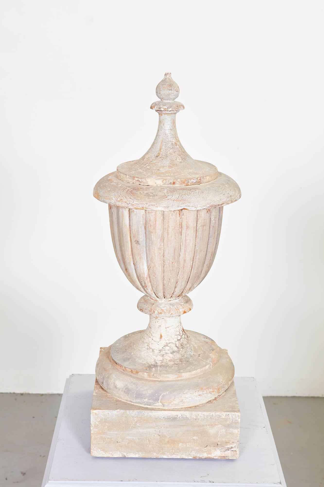A carved and painted 19th century classical urn with lobed body on footed base topped by turned cap and finial and featuring a superb patina. Now on new wooden plinth with paneled sides and molded top and base.
Urn dimensions: 10