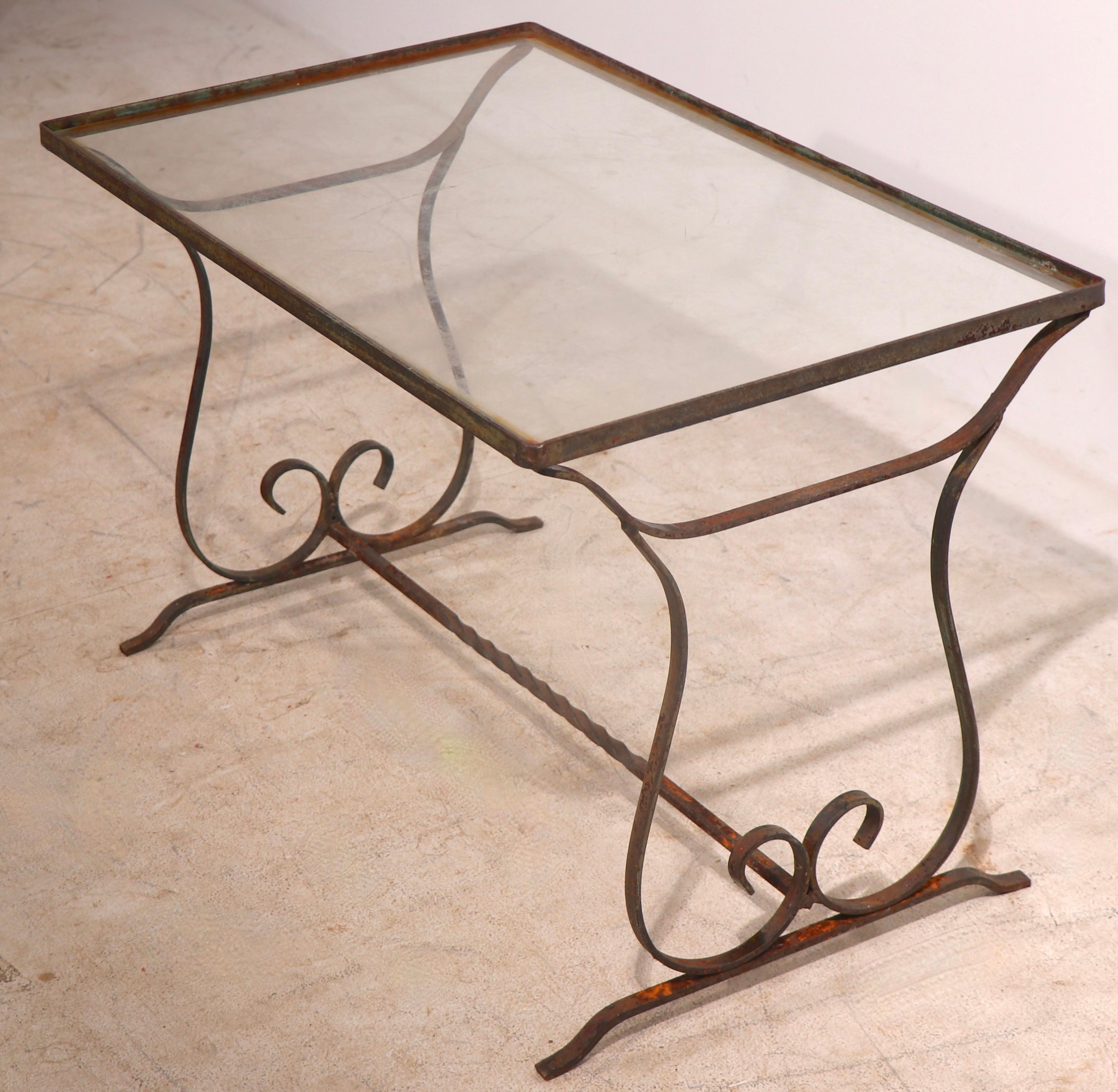 Charming diminutive garden, patio, poolside table of wrought iron and glass. The table features opposing curlicue form supports, with a twisted metal center stretcher. The top is glass, which shows some minor imperfections, usable as is, or easily