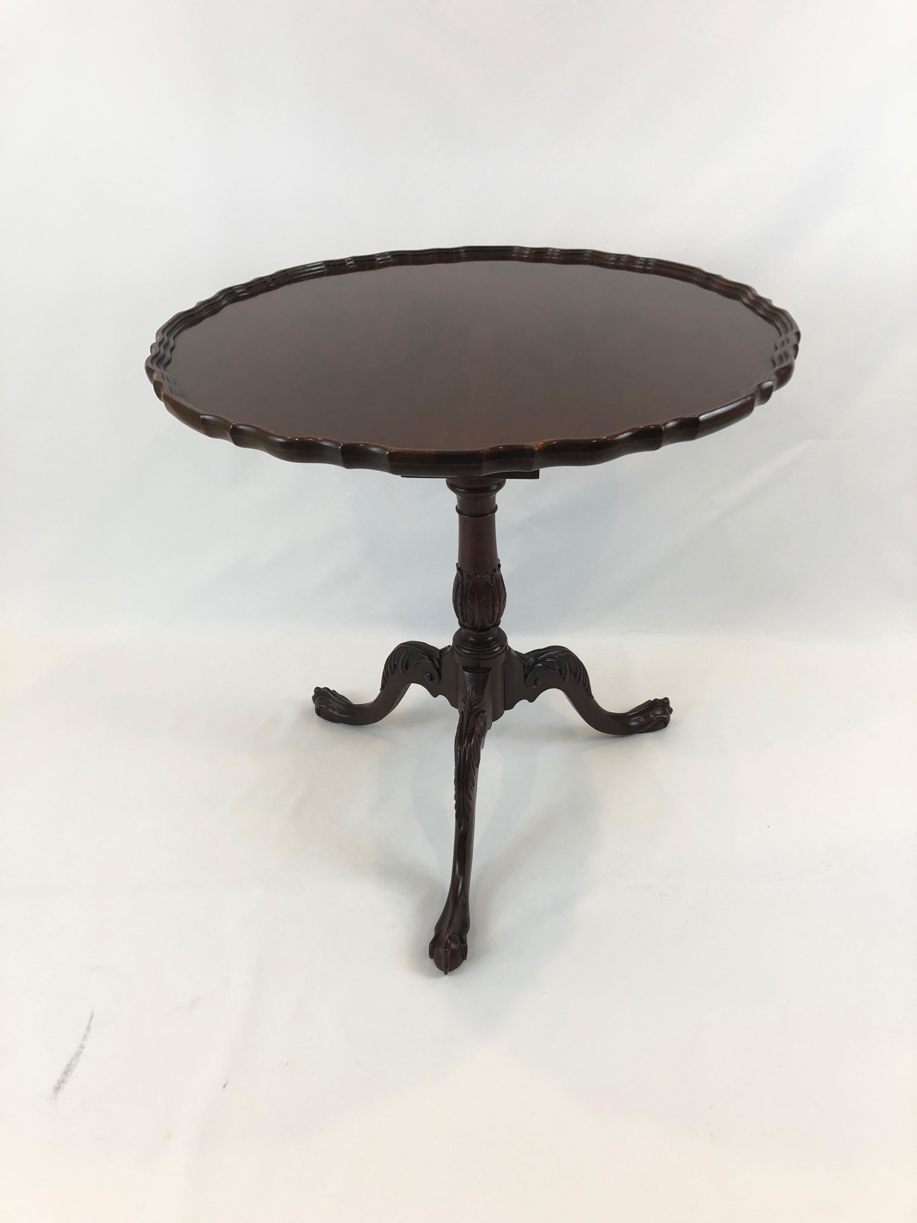 Traditional and timeless round tilt-top mahogany side table by Baker having a lovely pie crust edge, curved tripod legs and ball and claw feet.