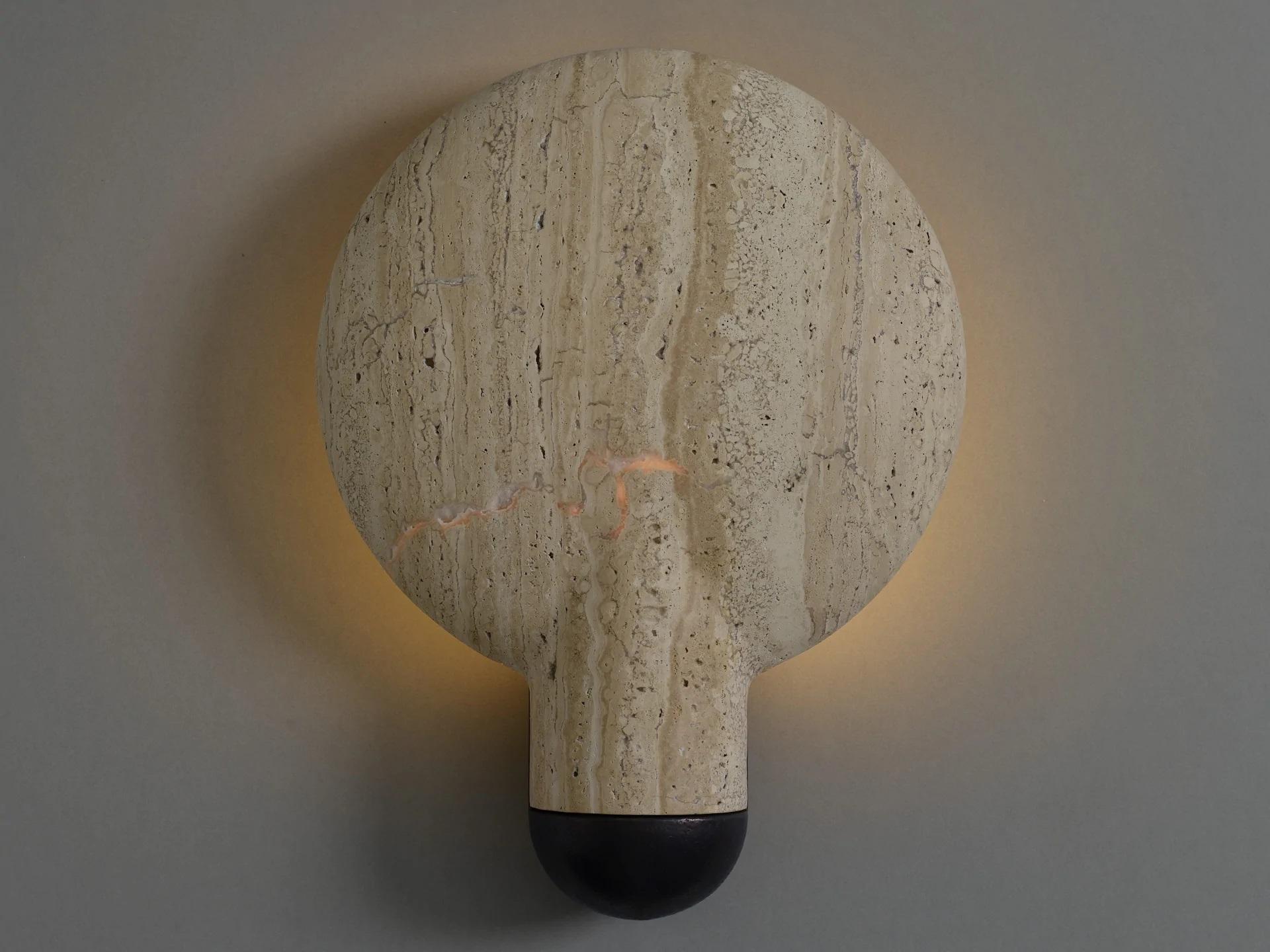 Classico Travertine wall sconce by Henry Wilson
Materials: travertine.
Dimensions: D 11 x W 30 x H 40 cm

Sandwiched between two components, the light source is projected onto the concave backing. The light follows the gentle bowl of the dish