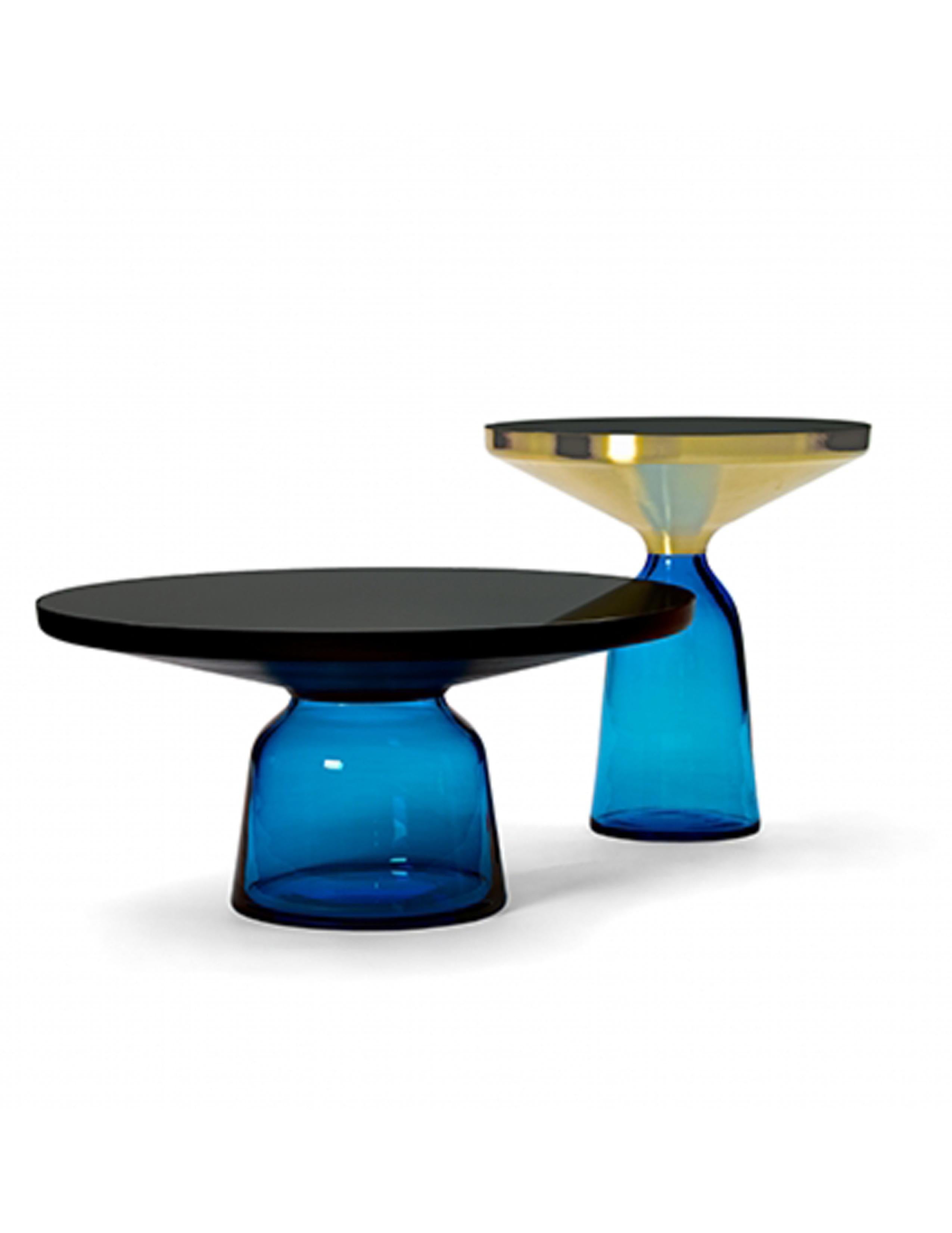 La table Bell de Sebastian Herkner bouleverse nos habitudes de perception en utilisant le matériau léger et fragile qu'est le verre comme base pour un plateau en métal qui semble flotter au-dessus. Soufflée à la main de manière traditionnelle à