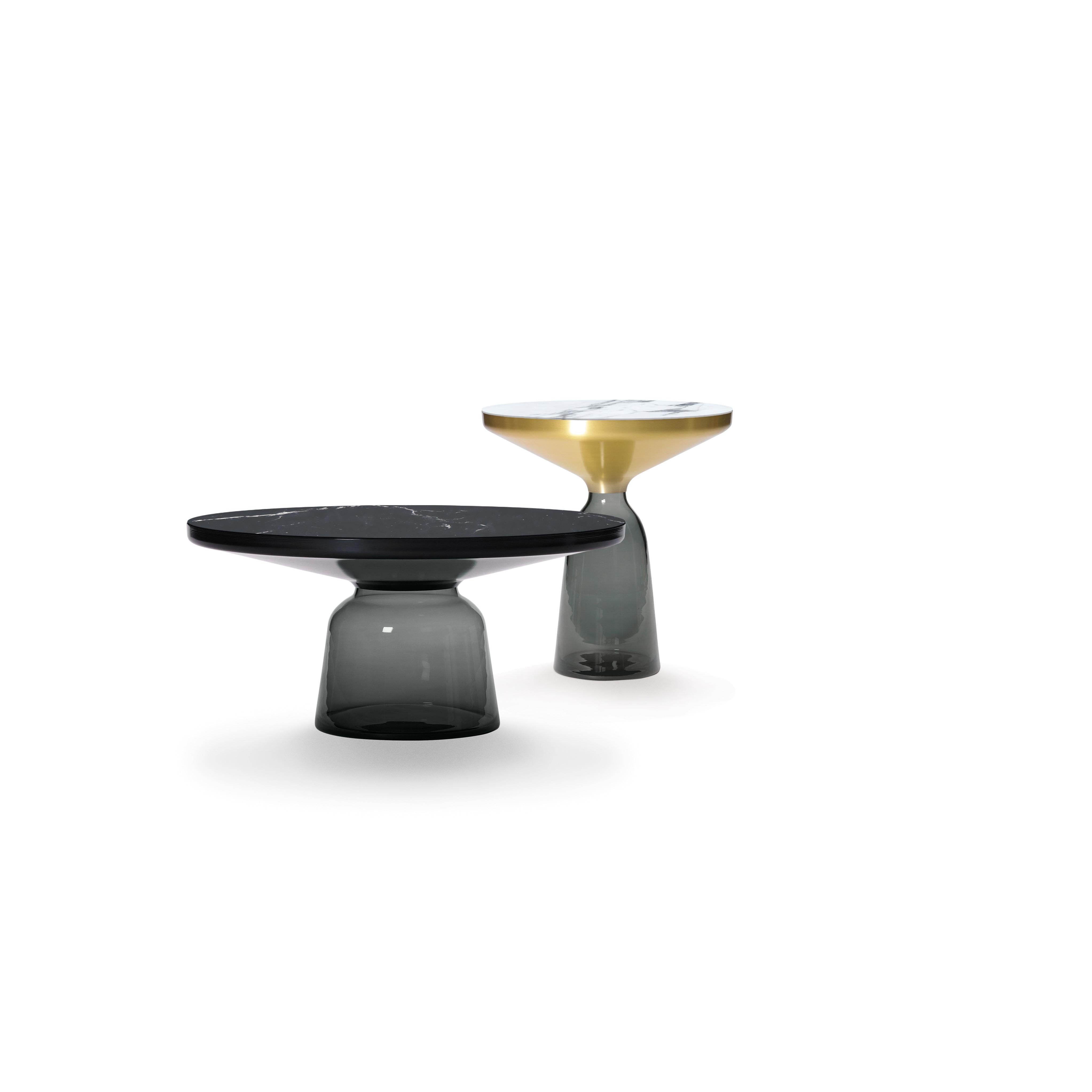 La table Bell de Sebastian Herkner bouleverse nos habitudes de perception en utilisant le matériau léger et fragile qu'est le verre comme base pour un plateau en métal qui semble flotter au-dessus. Soufflée à la main de manière traditionnelle à