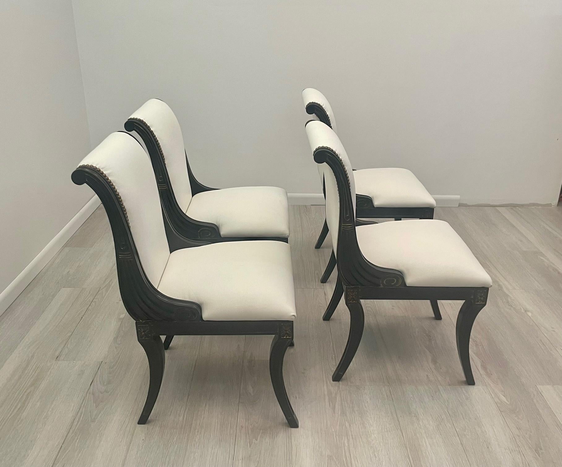Glamorous set of 4 ebonized wood Hollywood Regency side dining chairs upholstered in white leather and finished with brass nailheads. There are slight gilt highlights in the wood patina.
Measure: Seat height 18.