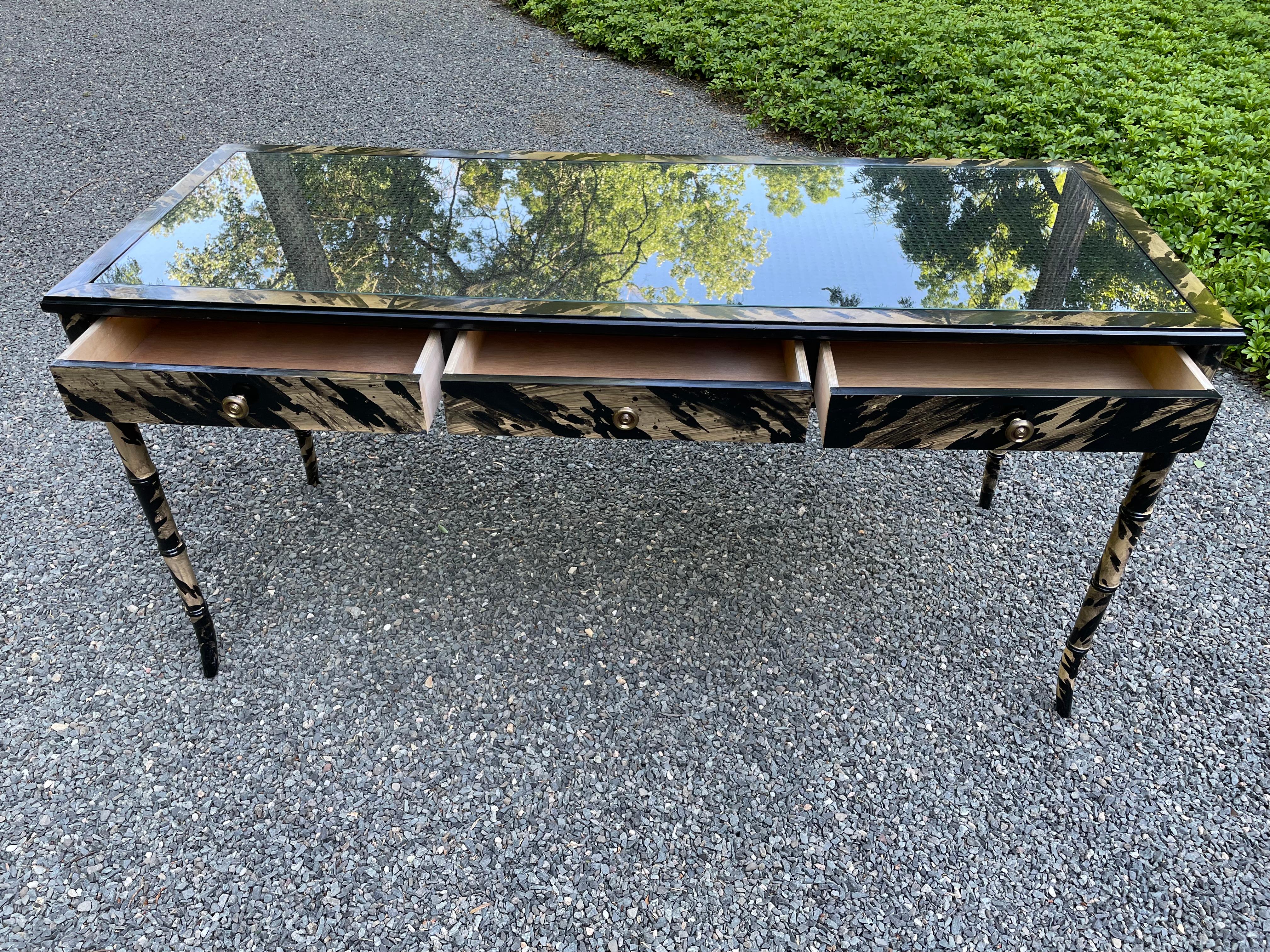 Very chic faux painted writing desk having 3 drawers and finished in a camel and black color palette. The lovely thin legs are shaped to resemble bamboo and the desk top is finished handsomely with black cane and inset glass on top.
knee clearance
