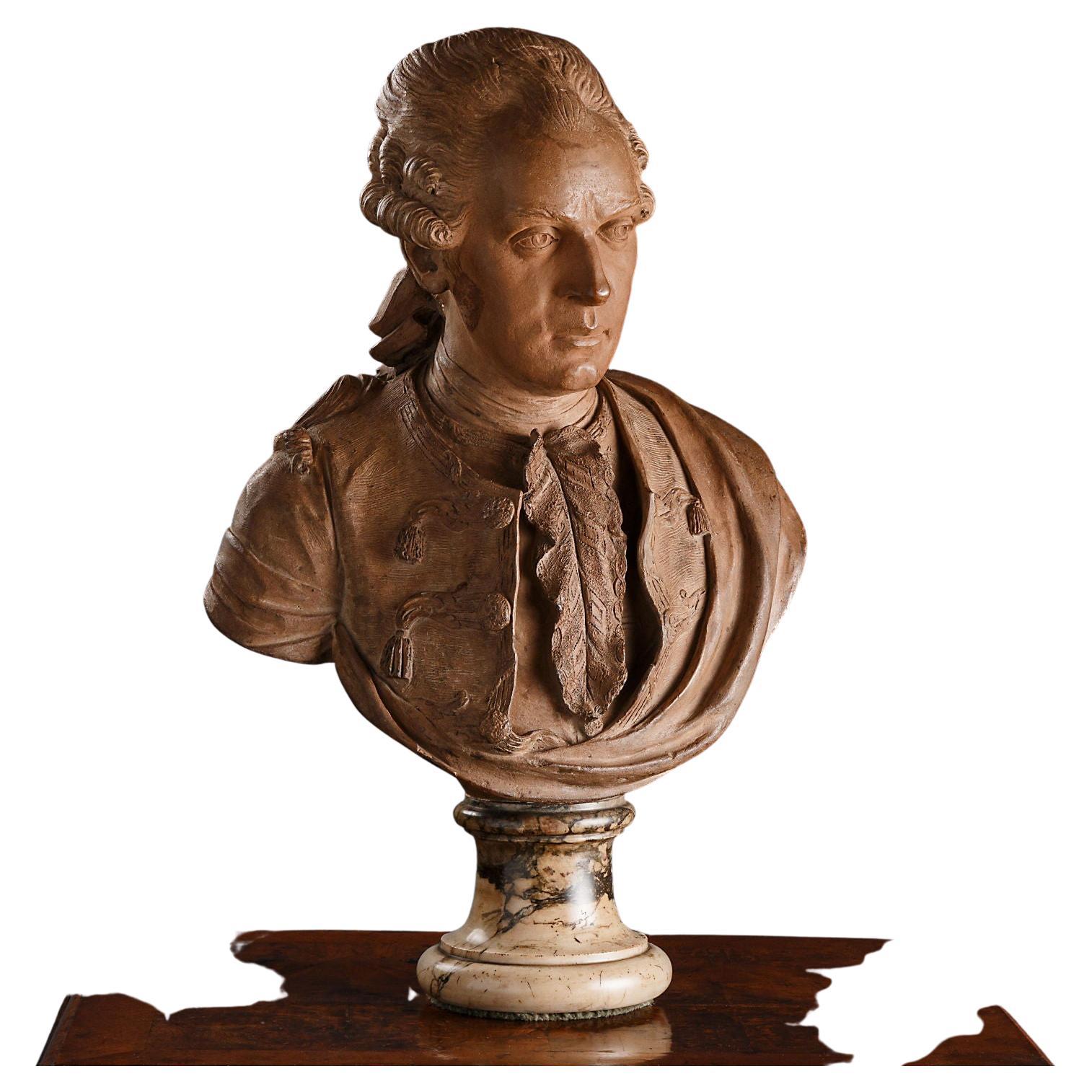 The terracotta bust, placed on a peduccio in colored marble, represents a male character with hair held in a tail by a ribbon and is dressed in a collarless tailcoat closed with frogs with applied tassels and embroidery along the edges, an