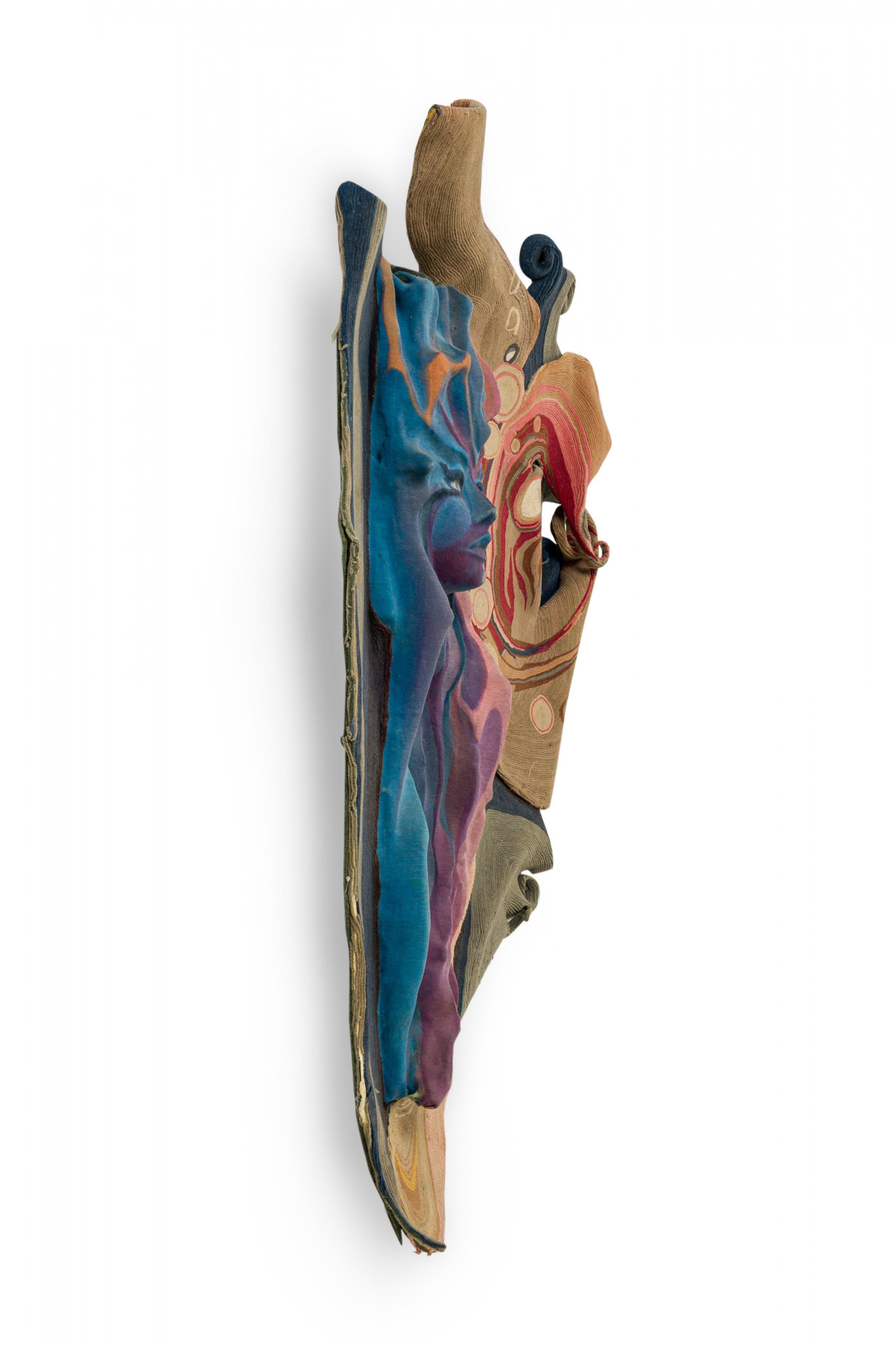 French midcentury (1970s) tapestry wall sculpture featuring abstract shapes in beige, red, green and gray, surrounding dimensional face in blues and purples. (Claude Prevost).
