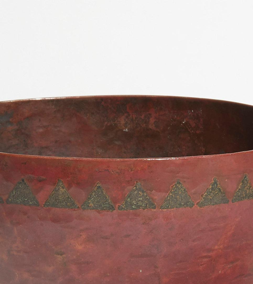 A Dinanderie flared-shape cup with red patina, the decor with silvered triangles friezes on the border, resting on a small circular base in wrought iron
Signed.