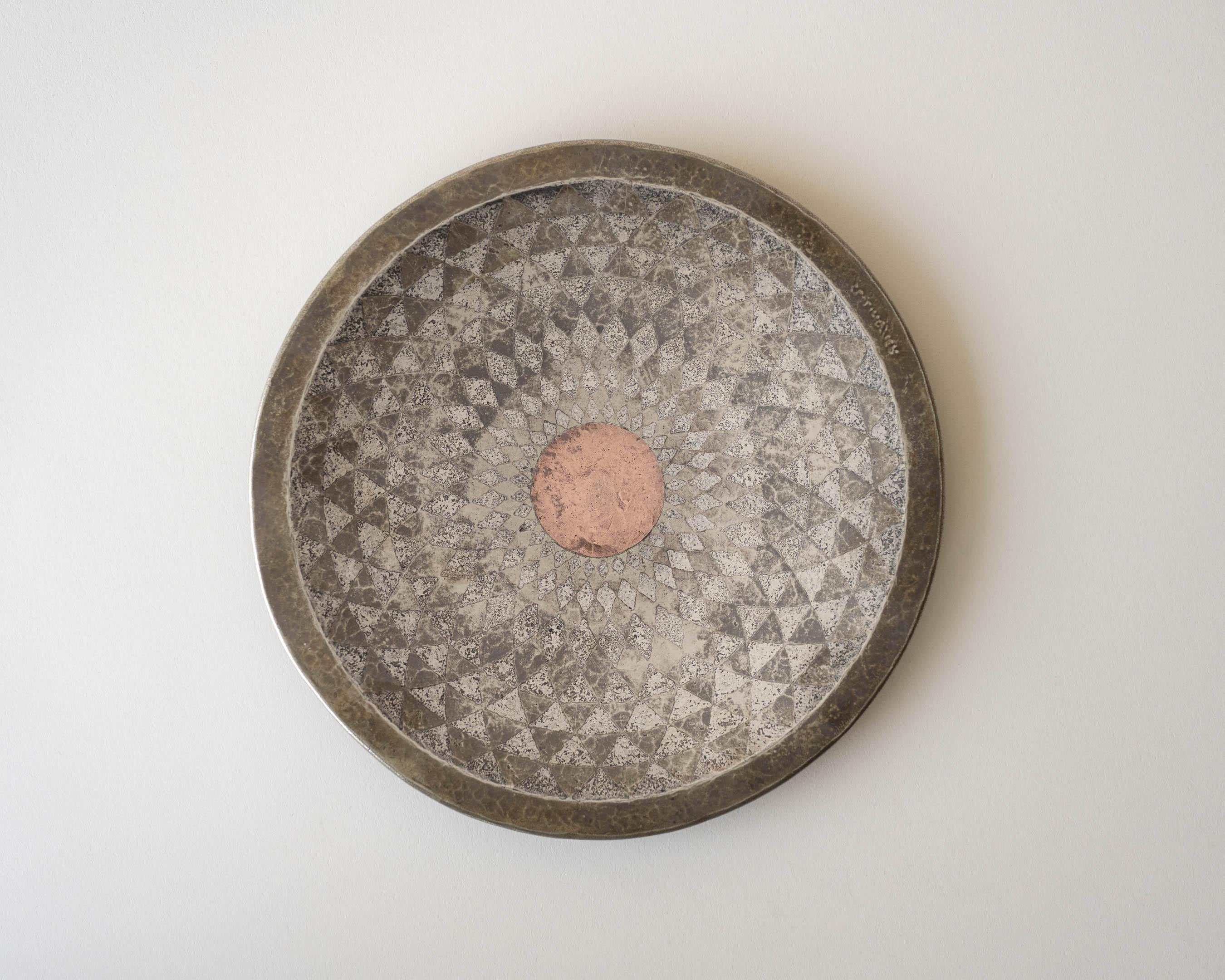 A small, hammered dinanderie charger with radiating geometric decor in patinated silver and copper. Signature 