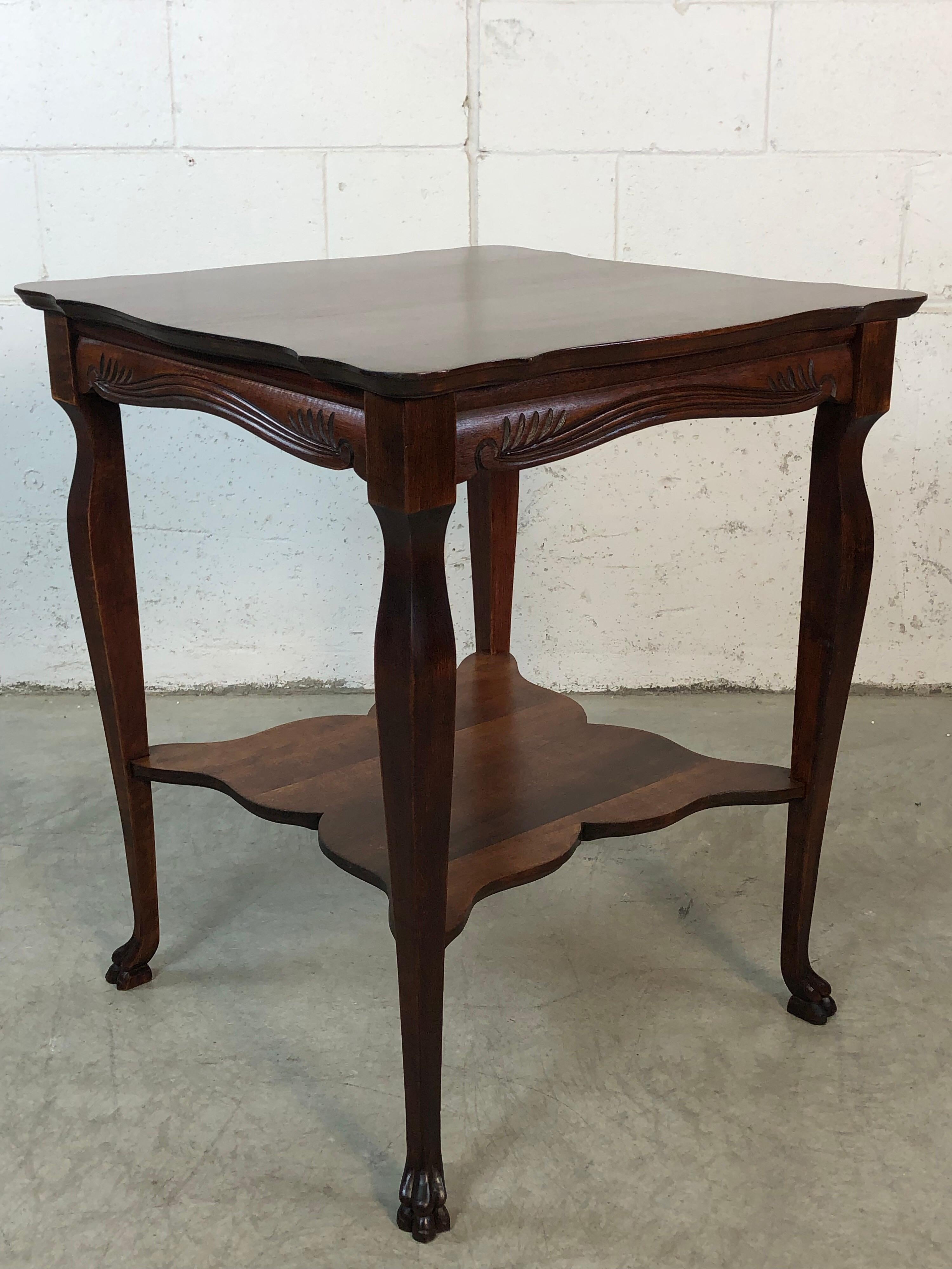 1930s square hand carved wood side table. The table has carved claw feet and carved accents along the skirt. The top of the table has a scalloped edge. The table is in fully restored condition.