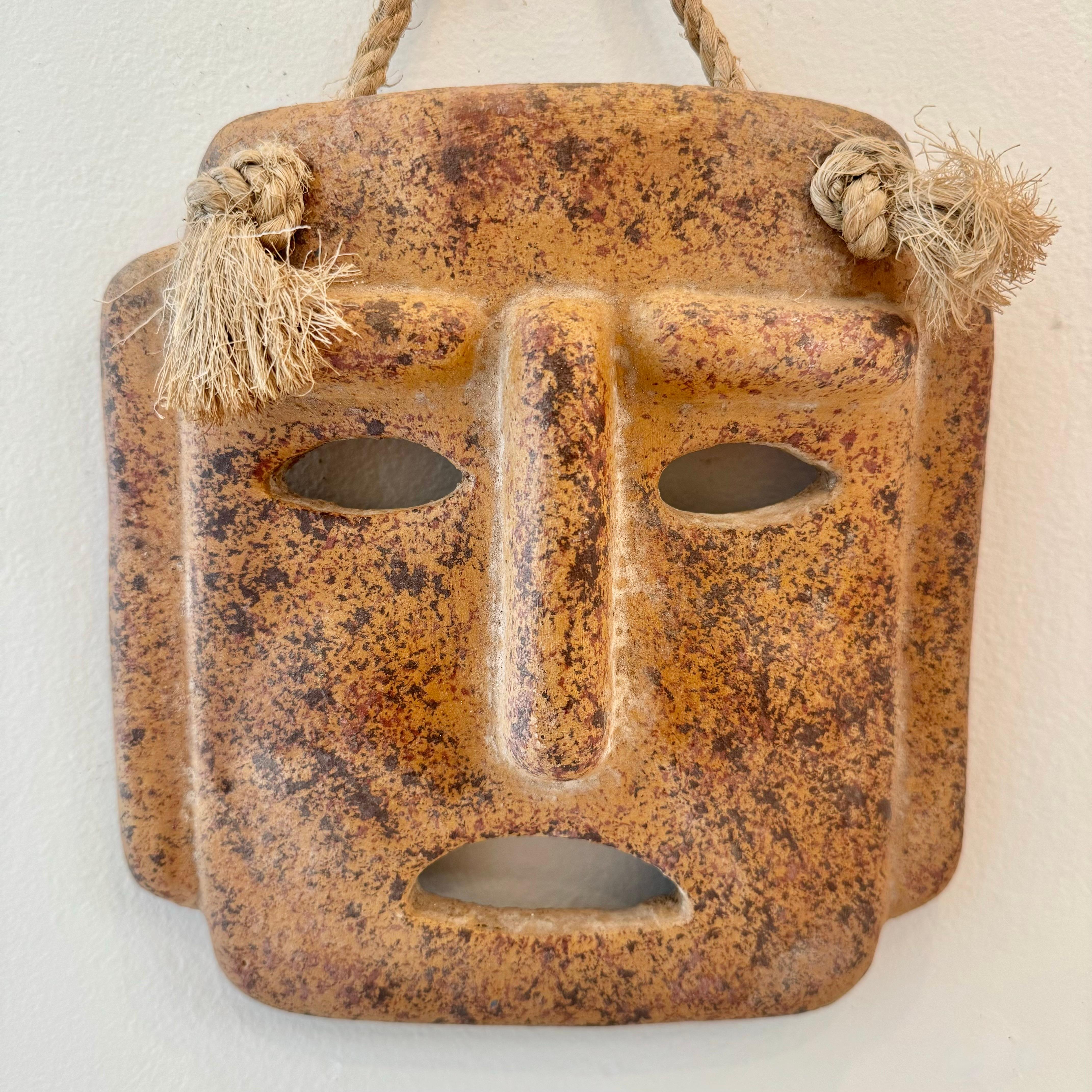 Fantastic sculptural clay mask wall art made in Italy. Hand made in an aged adobe color with a short rope which ties off on the face of the mask. Hangs from a single screw making install simple. Gorgeous piece of art for the wall or on a table.