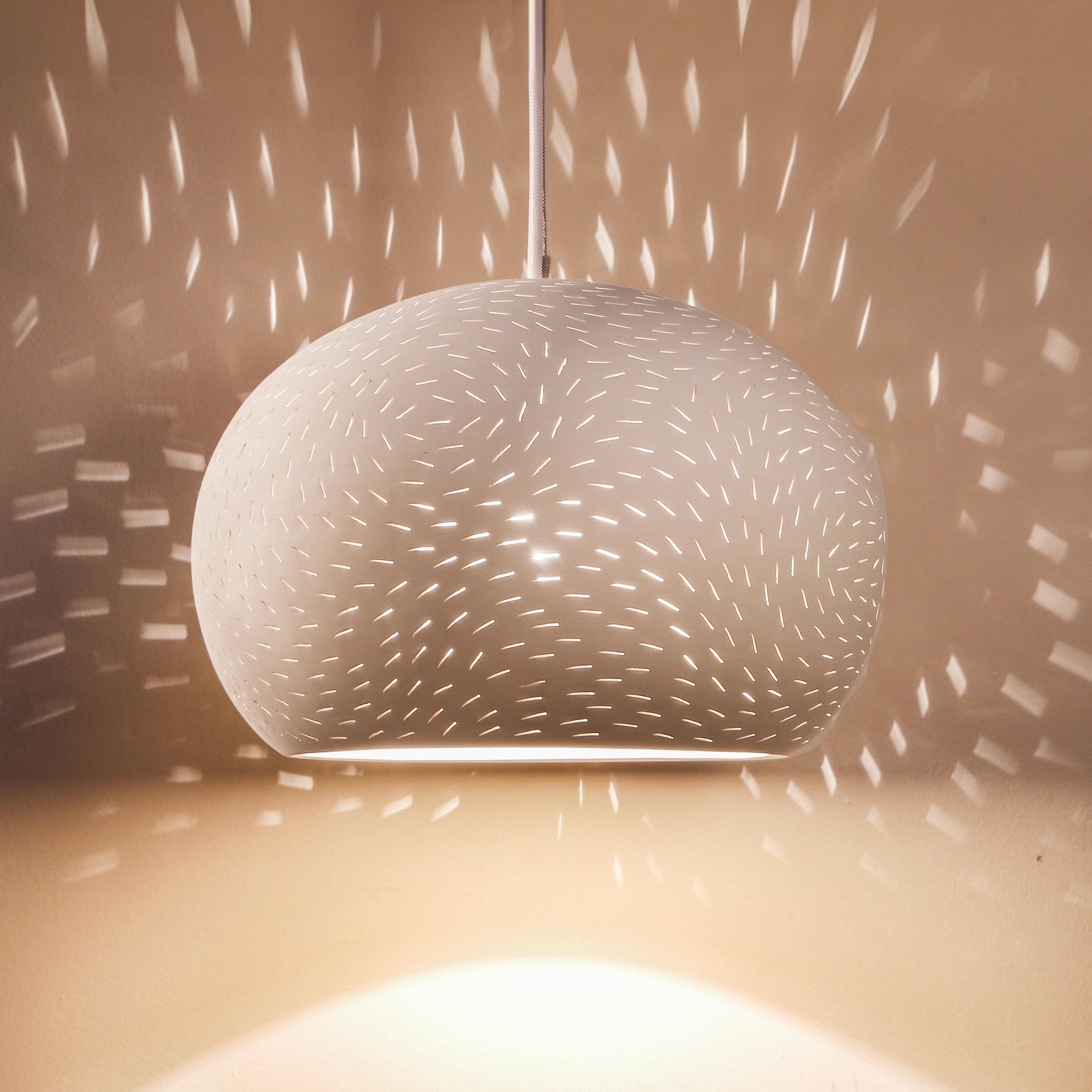 A perforated white ceramic pendant light with an elegant braided cord and a matching ceramic ceiling plate.

We offer this light in two perforation patterns: Lines or Dots. Option available to order both LED and Incandescent bulbs.
Projects light