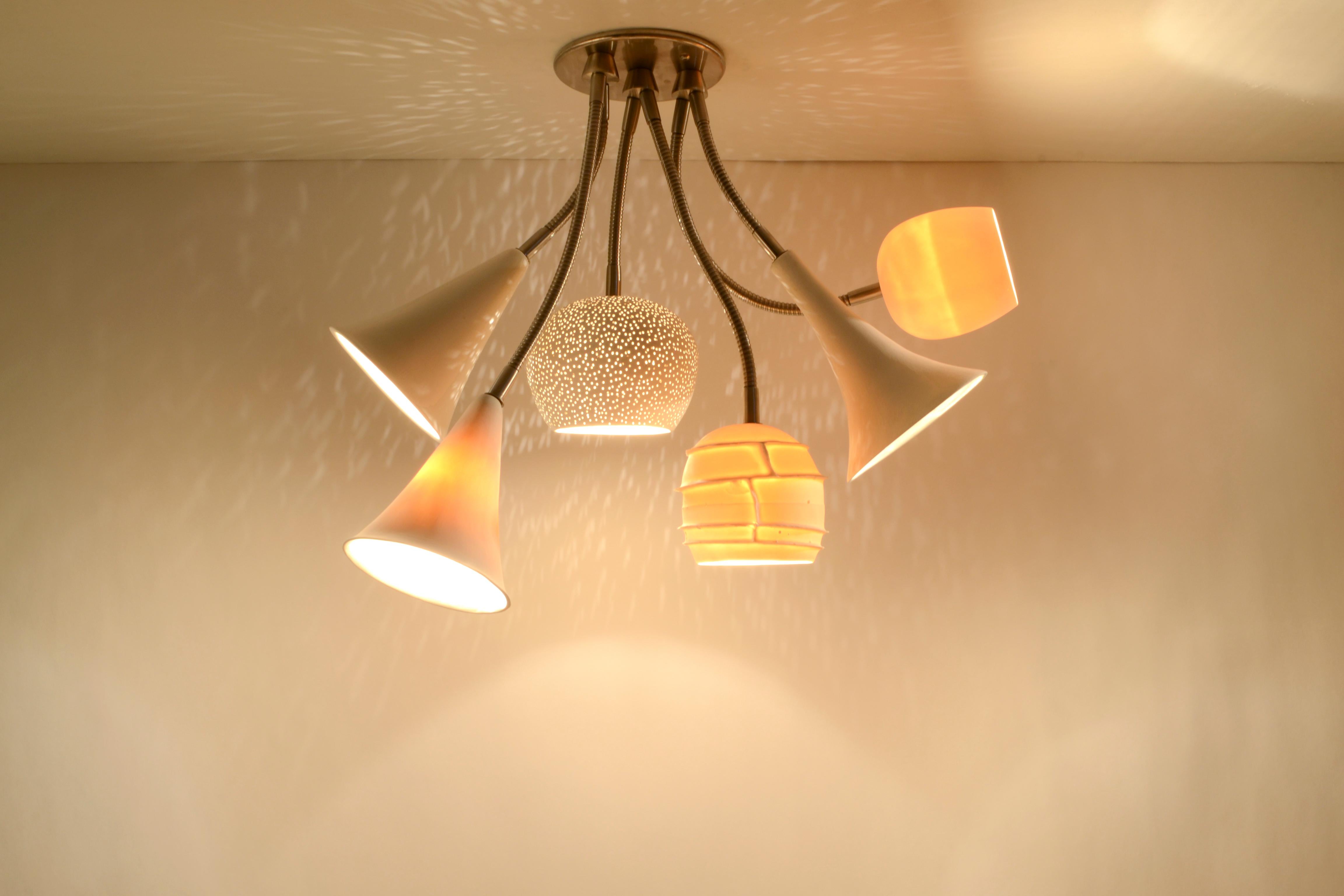 This cluster chandelier was inspired by the idea of a radiant floral arrangement. It is crafted from a variety of warm white matte ceramic and porcelain shades. One ceramic shade is hand-perforated, creating a starry-night effect when it's on, while