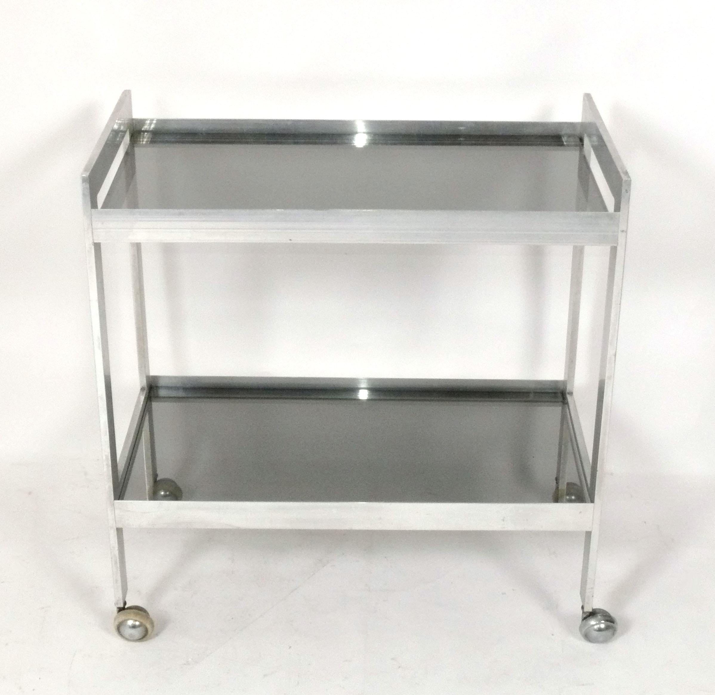 Clean Lined Mid Century Aluminum Bar Cart, American, circa 1960s. It is constructed of aluminum with light gray glass shelves. It is a versatile size and can be used as a bar cart, or as rolling storage in a home office.