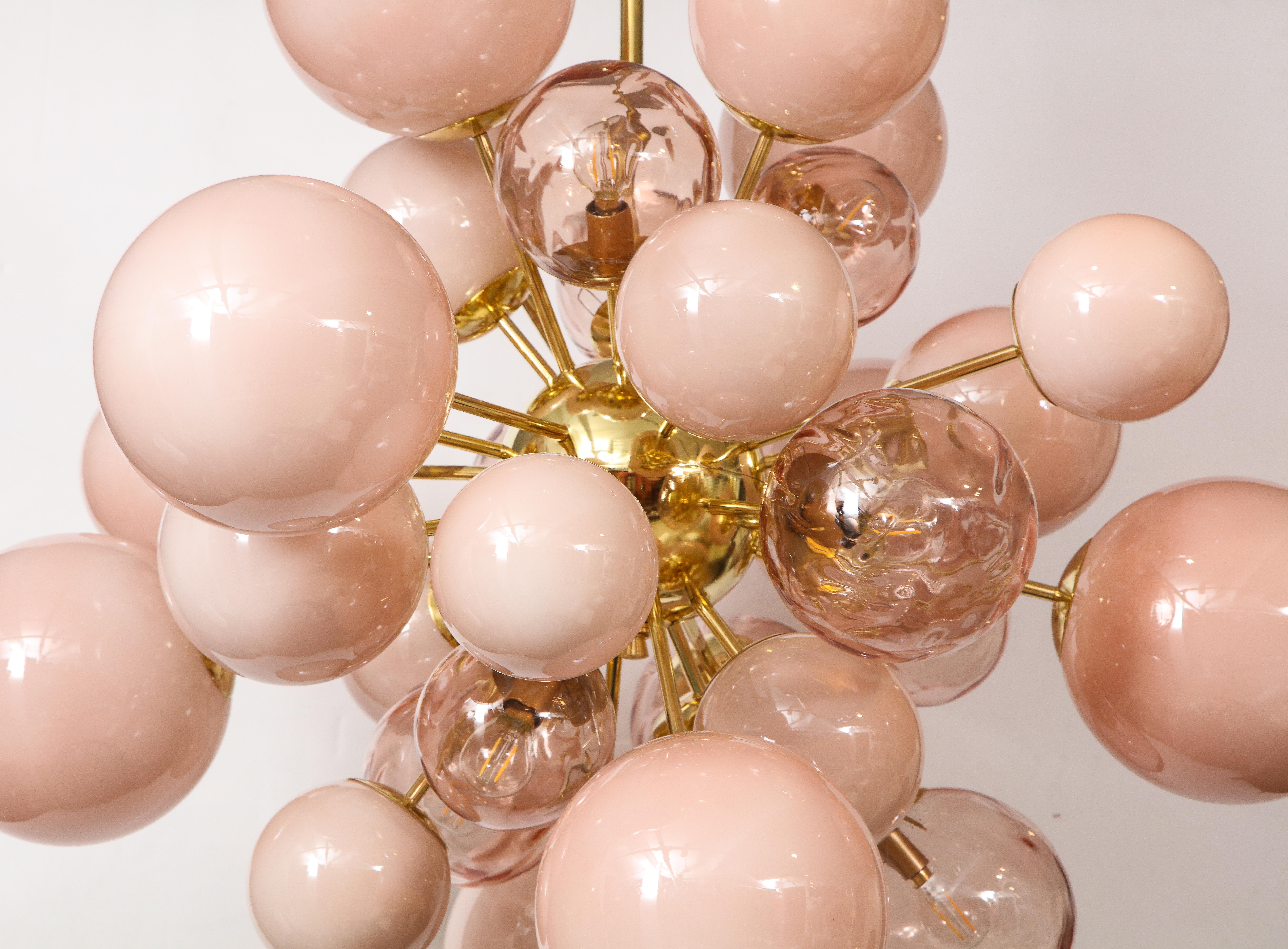 Unique sputnik or starburst chandelier consisting of hand blown, pink blush Murano glass globes or spheres of various sizes in both clear and opaque glass finish. Each glass globe is connected to a brass rod which radiates from a brass center sphere