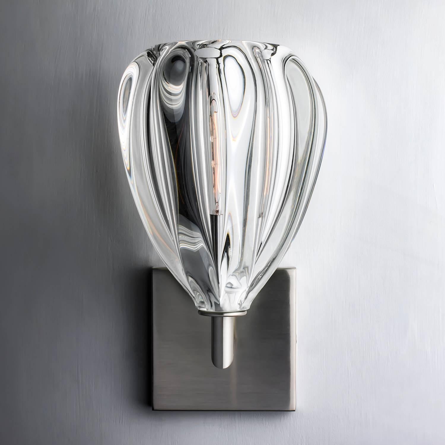 This series of wall sconces is classically inspired. Scaled versions of our pendants extend from elegant metal armatures. The proximity of the glass to the wall allows for each piece’s unique light pattern to be magnified. Hand blown and shaped in