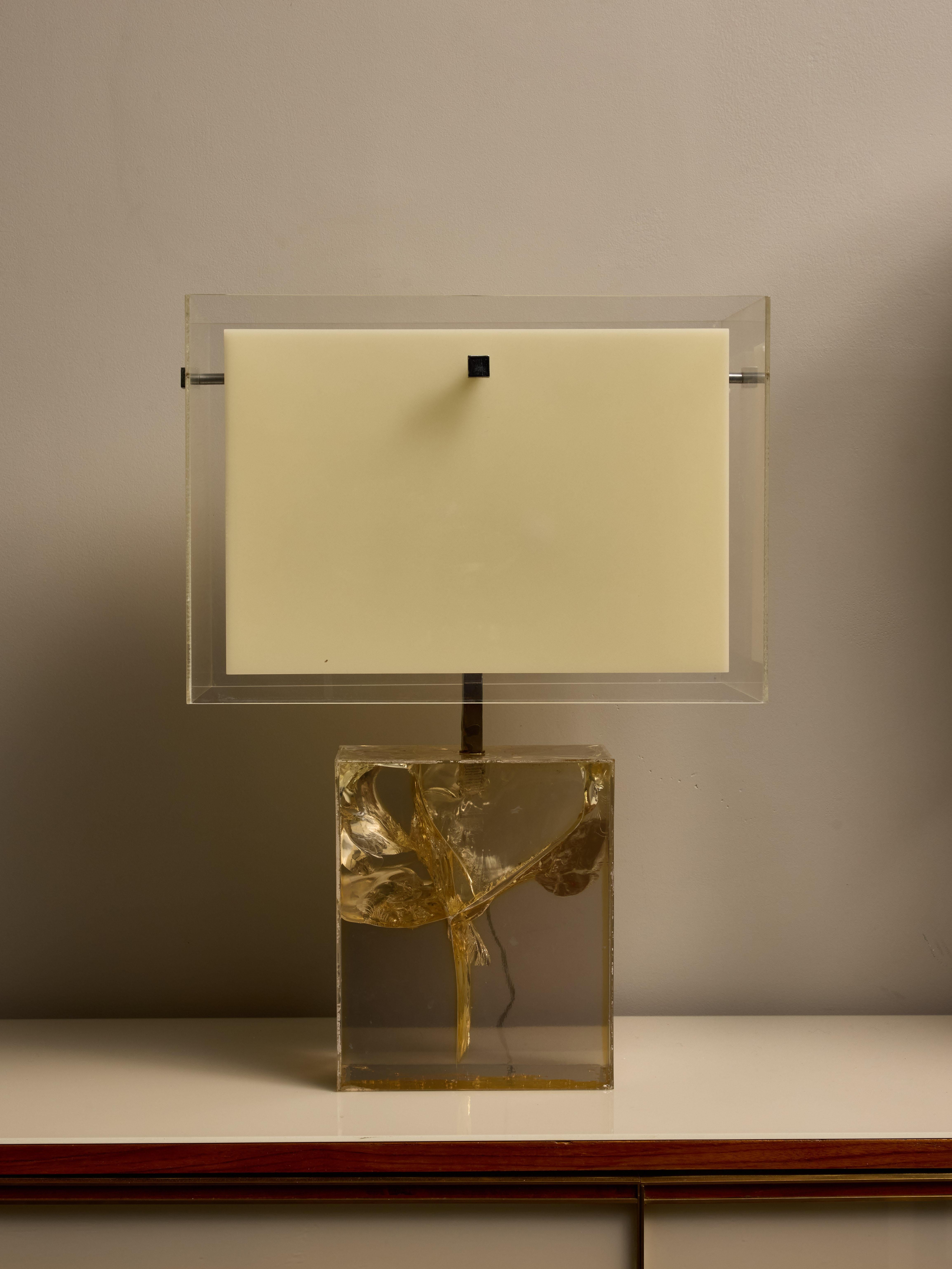 A transparent fractal resin rectangular table lamp features a chrome central stem that supports dual-layer shades made of acrylic. The inner layer is white, effectively diffusing the light and concealing the bulbs, while the outer layer has a