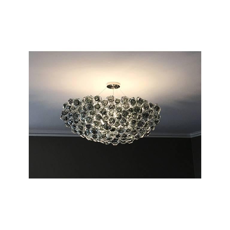 An ensemble of hand-sculpted glass elements come together to form an organic yet solid sculptural form. Cable suspension from 5” diameter ceiling canopy. Internal three-way, medium base socket illumination. 

Measures: 38” diameter x 15” height.