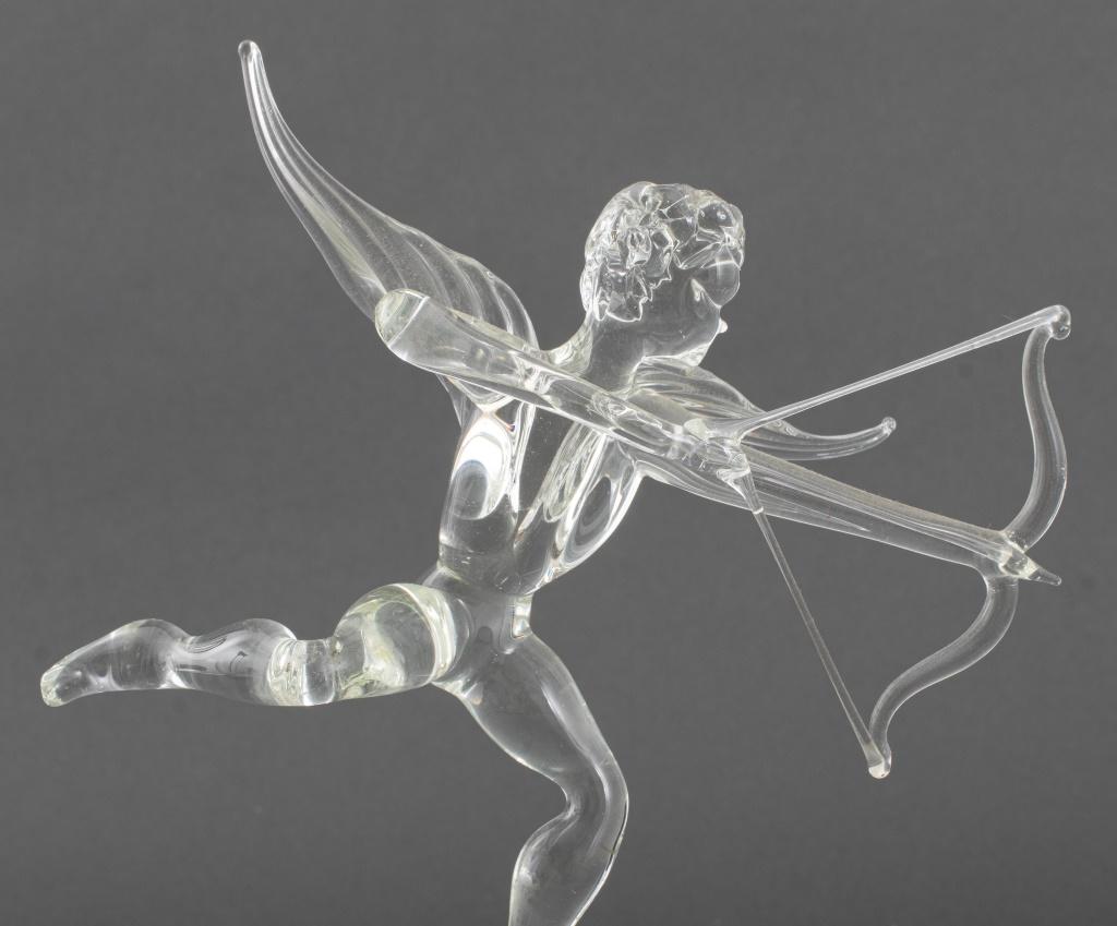 Clear Glass Cupid Figurine holding bow and arrow balancing on three leg stand.

Dealer: S138XX