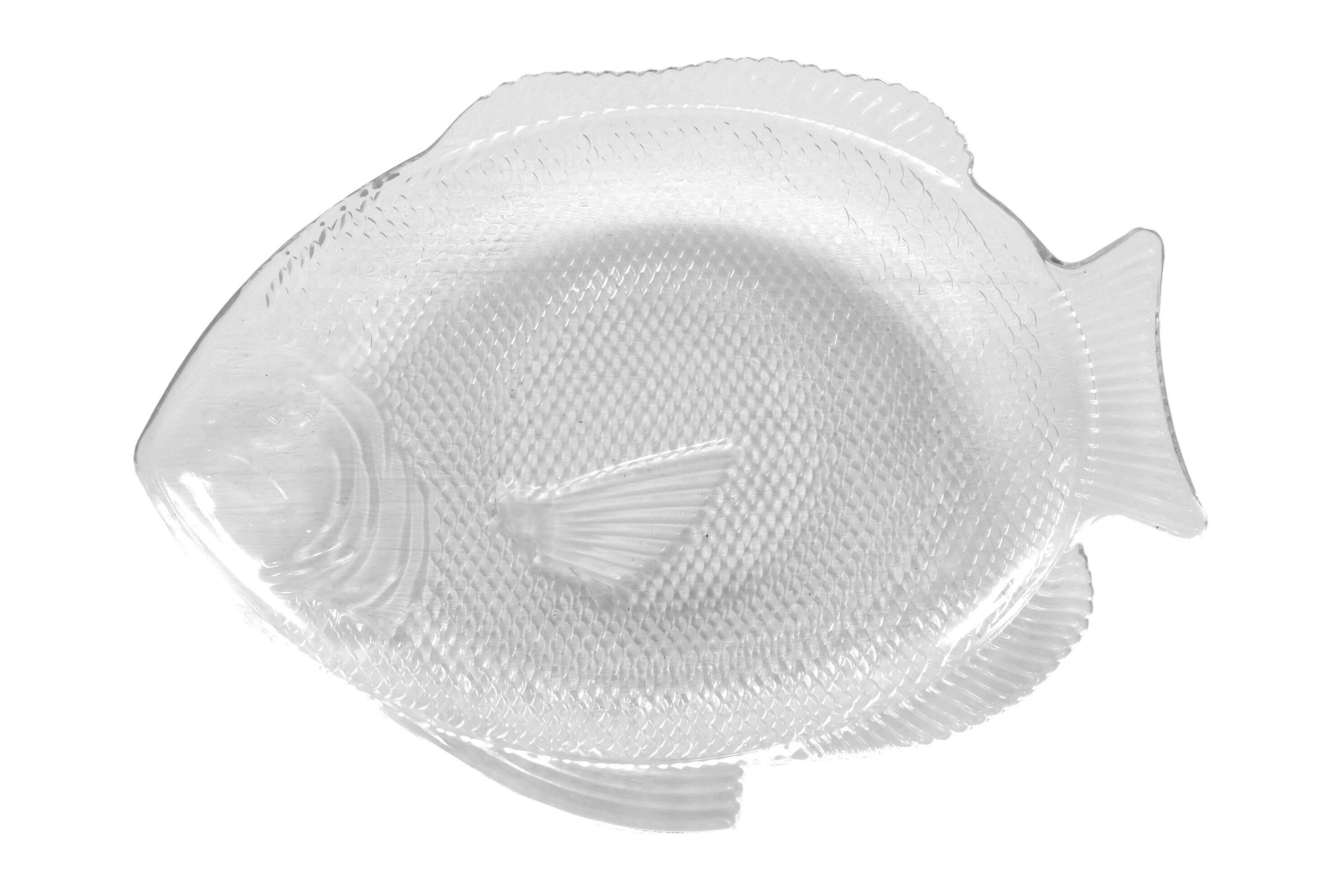 Un plat en verre transparent en forme de poisson. Pressé avec des écailles et des lignes pour montrer les détails tels que les yeux et la bouche sur la tête et des lignes pour montrer les nageoires. Marqué en dessous 