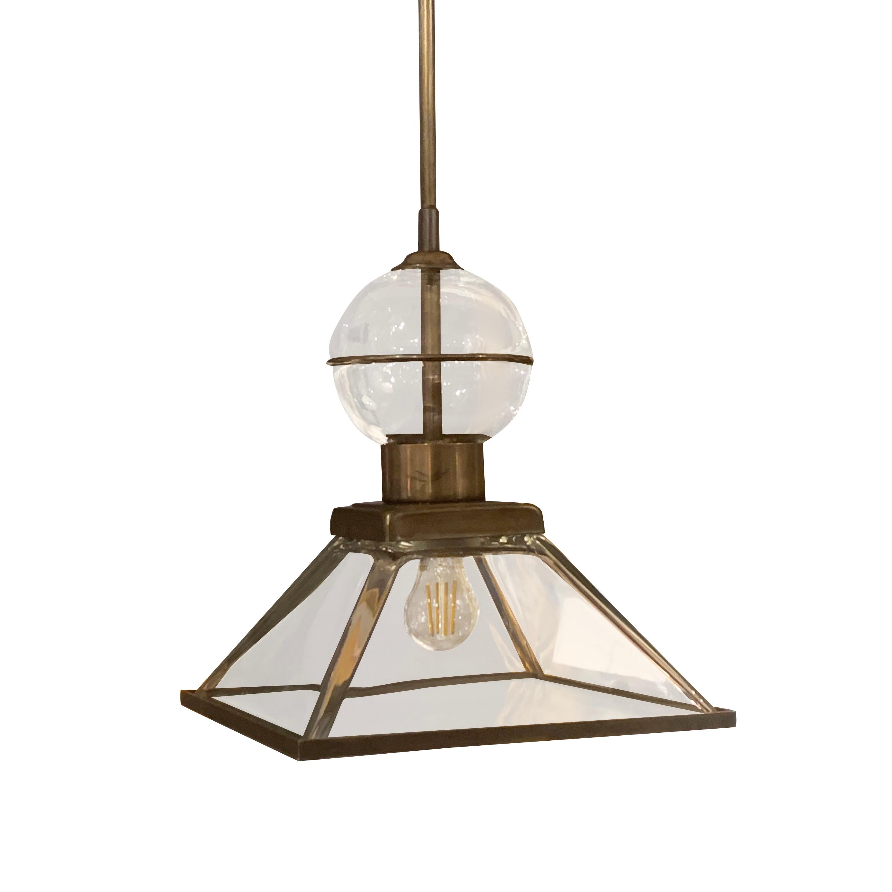 Contemporary Italian square glass pendant lights.
Decorative glass sphere sits atop the pyramid shaped fixture.
Brushed brass surrounding the glass, rod and canopy.
These square glass pendants can be ordered in multiples.
Fixture only height is