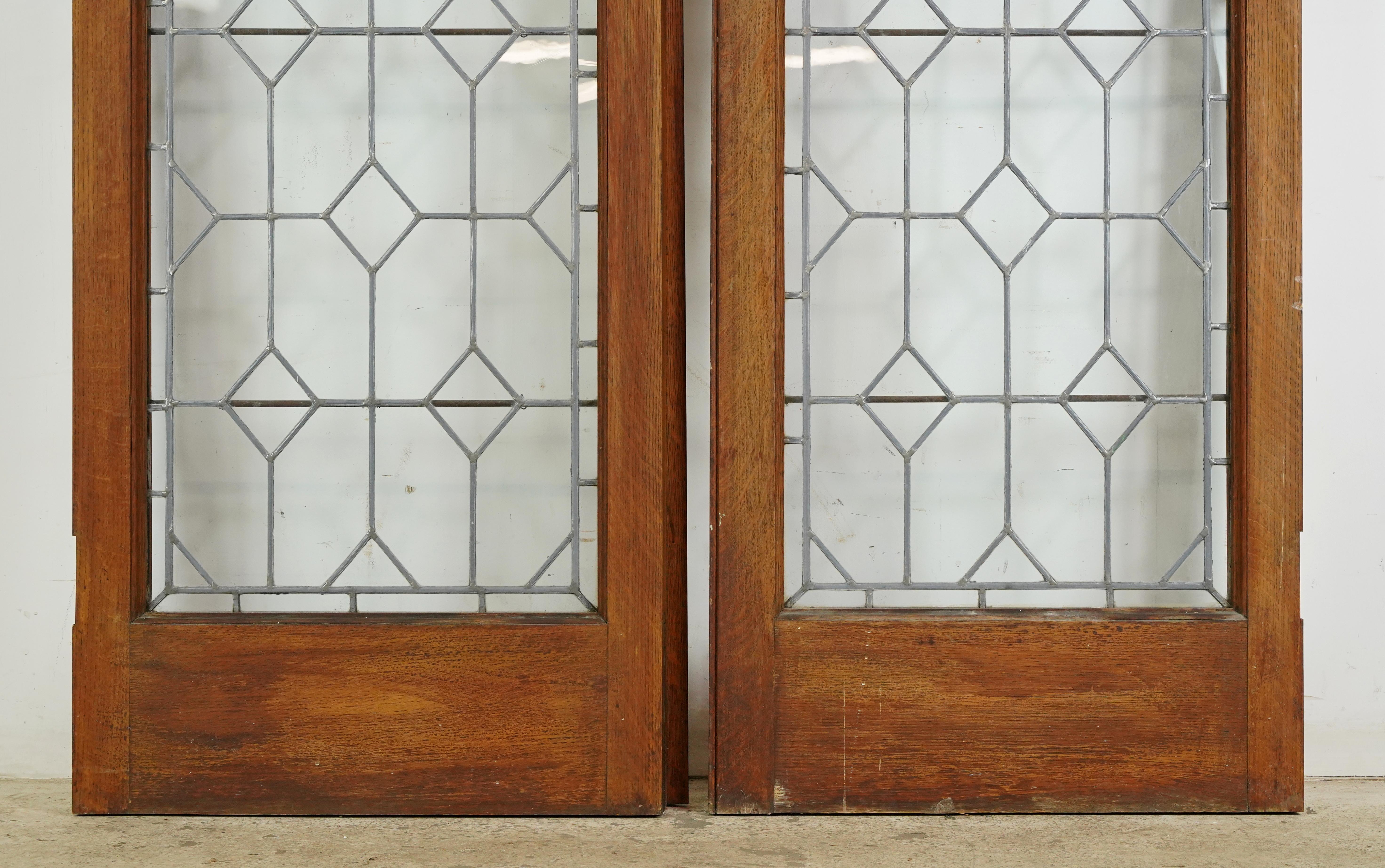 Passage double doors with clear leaded glass in a geometric pattern and dark wood tone oak frames. There is some wear on the bottoms and sides, and a small crack. Priced as a double. Some original hardware is still attached. Please note, this item