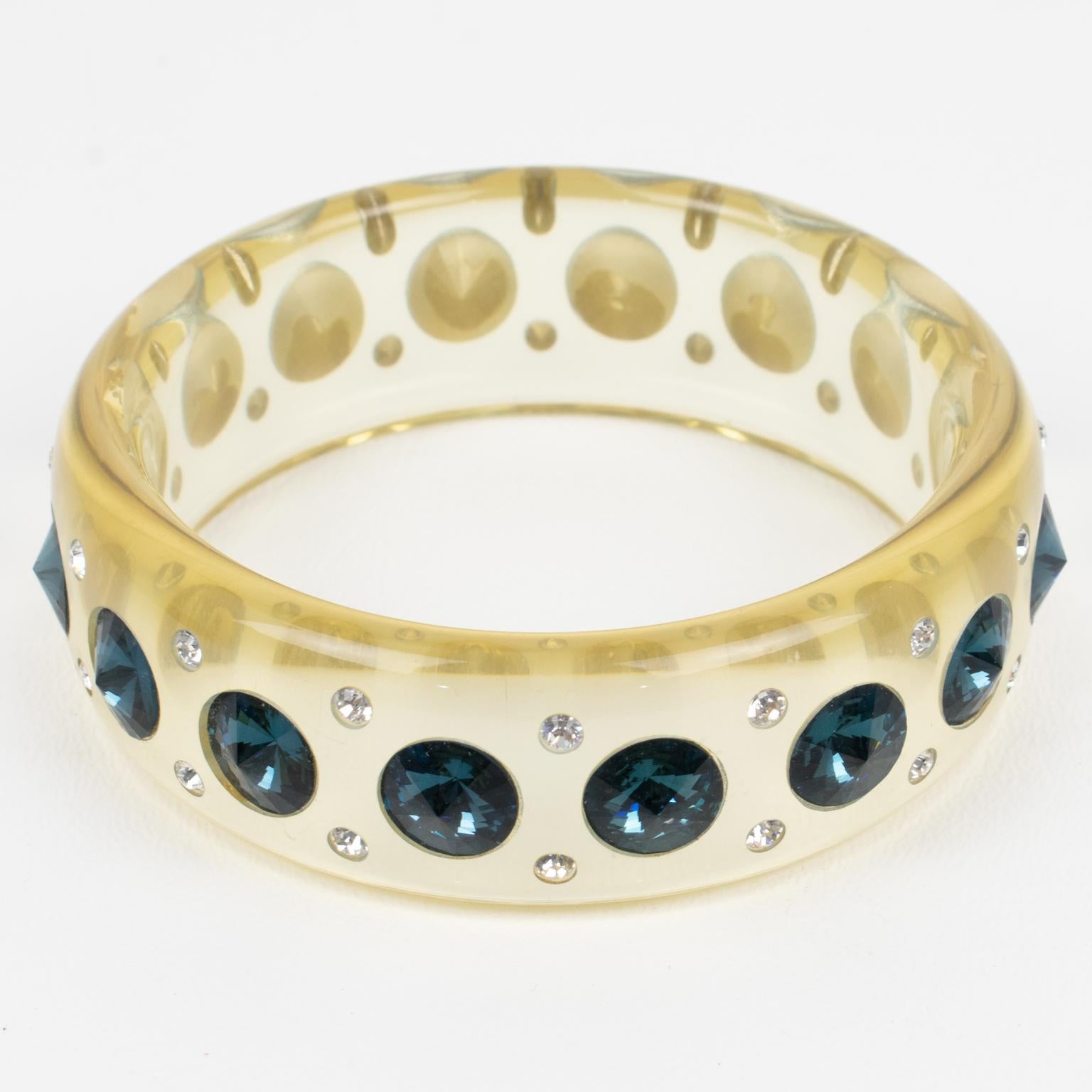 Ce superbe bracelet en Lucite présente une forme bombée de couleur jaune pâle transparente. Le bracelet est orné de strass massifs en cristal bleu denim et de minuscules strass argentés. Il n'y a pas de marque de fabricant visible.
Mesures :