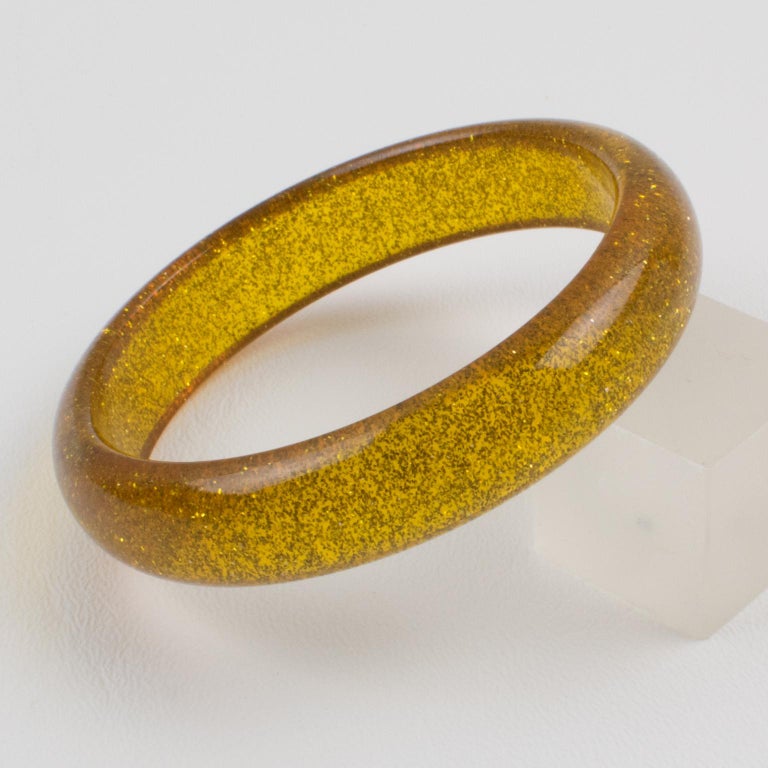 Charming Lucite bracelet bangle. The bangle has a domed shape and is comprised of transparent yellow marigold Lucite which is injected with metallic confetti inclusions in gold color. The metallic confetti glitter like those of Christmas
