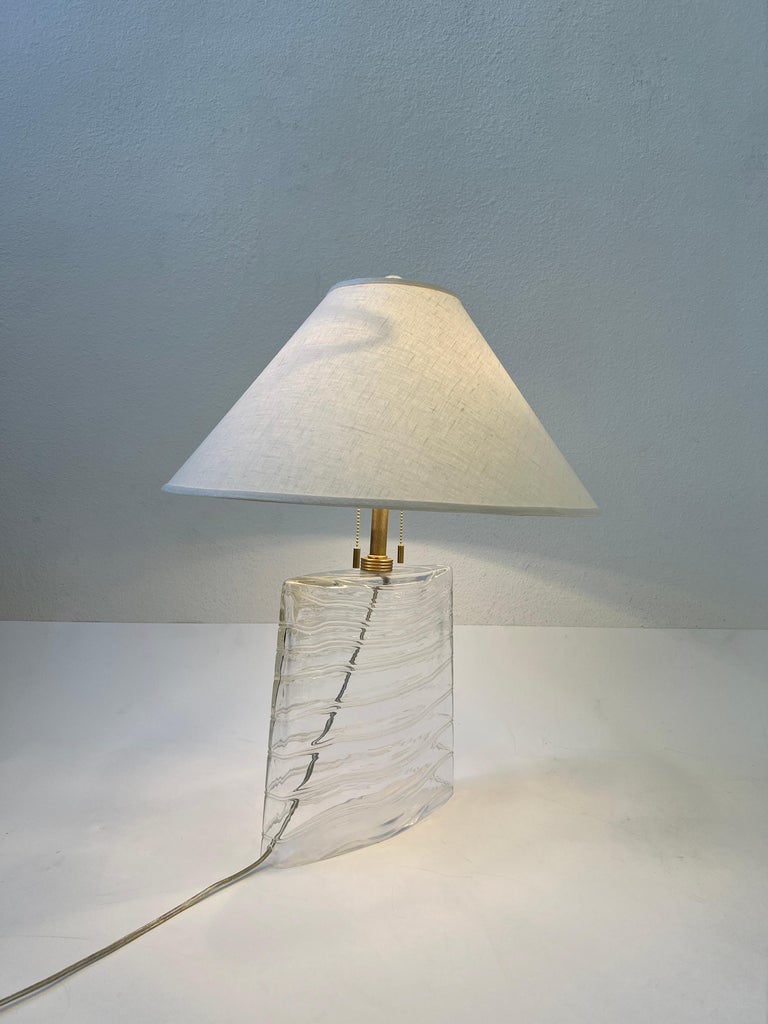 Glamorous 1980’s clear Murano glass and satin brass table lamp designed by John Hutton for Donghia. The lamp is signed on the bottom, where the cord comes out(see detail photos).
Newly rewired and new vanilla linen shade. 
It takes two 75w max