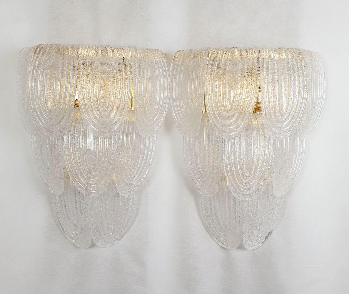 Mid-Century Modern pair of large Murano glass sconces, attributed to Mazzega, Italy 1970s.
The Italian sconces have a neoclassical style, and are very elegant and quality.
The vintage pair of sconces is made of translucent clear Murano glass and a