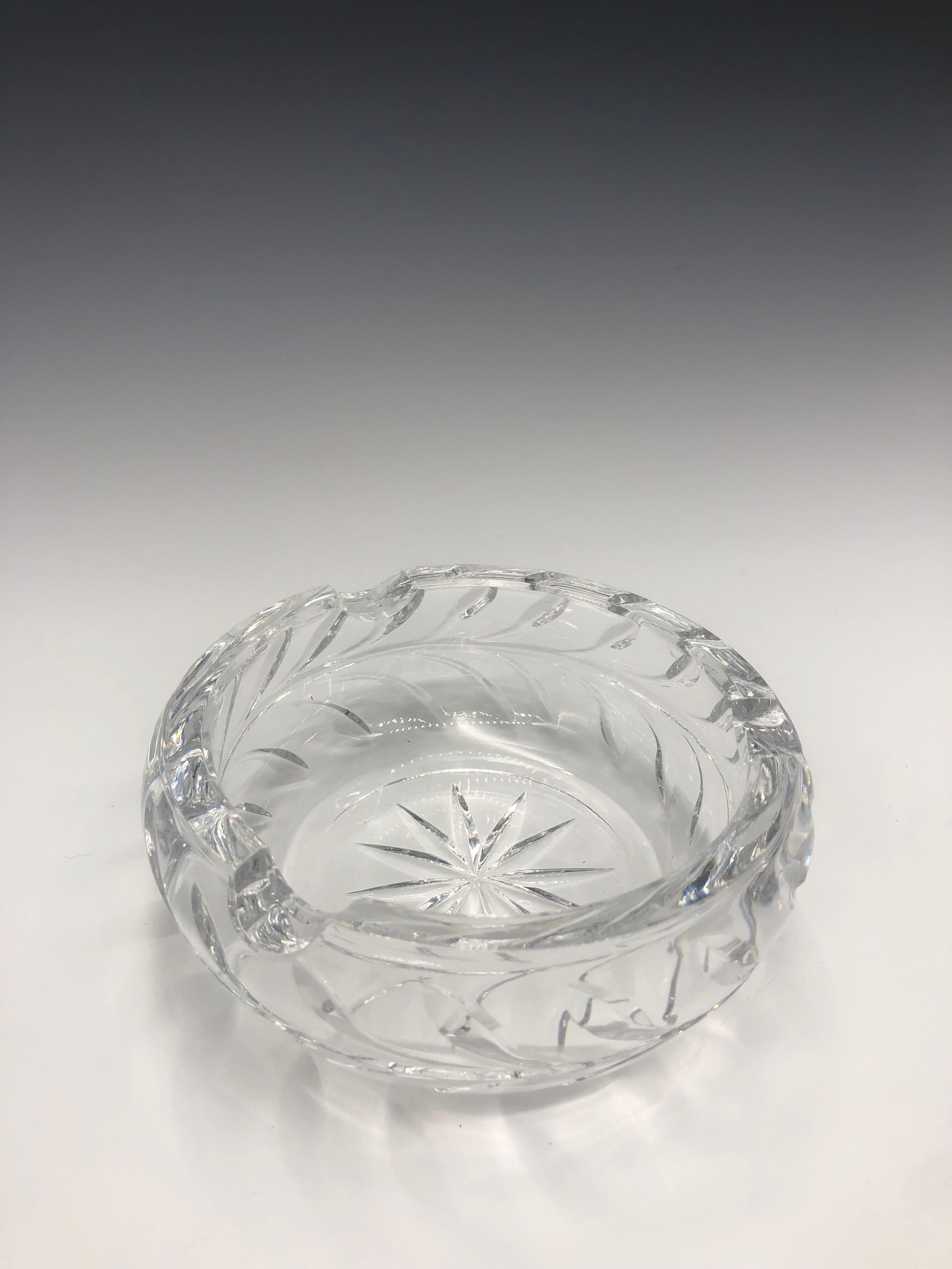 Clear thick unmarked round crystal cut glass ashtray in perfect condition. 

It has a star/sunburst cut motif in the center with leaf-cut design detail around the edges. 

It is a pretty decorative tabletop piece that can also be used as a