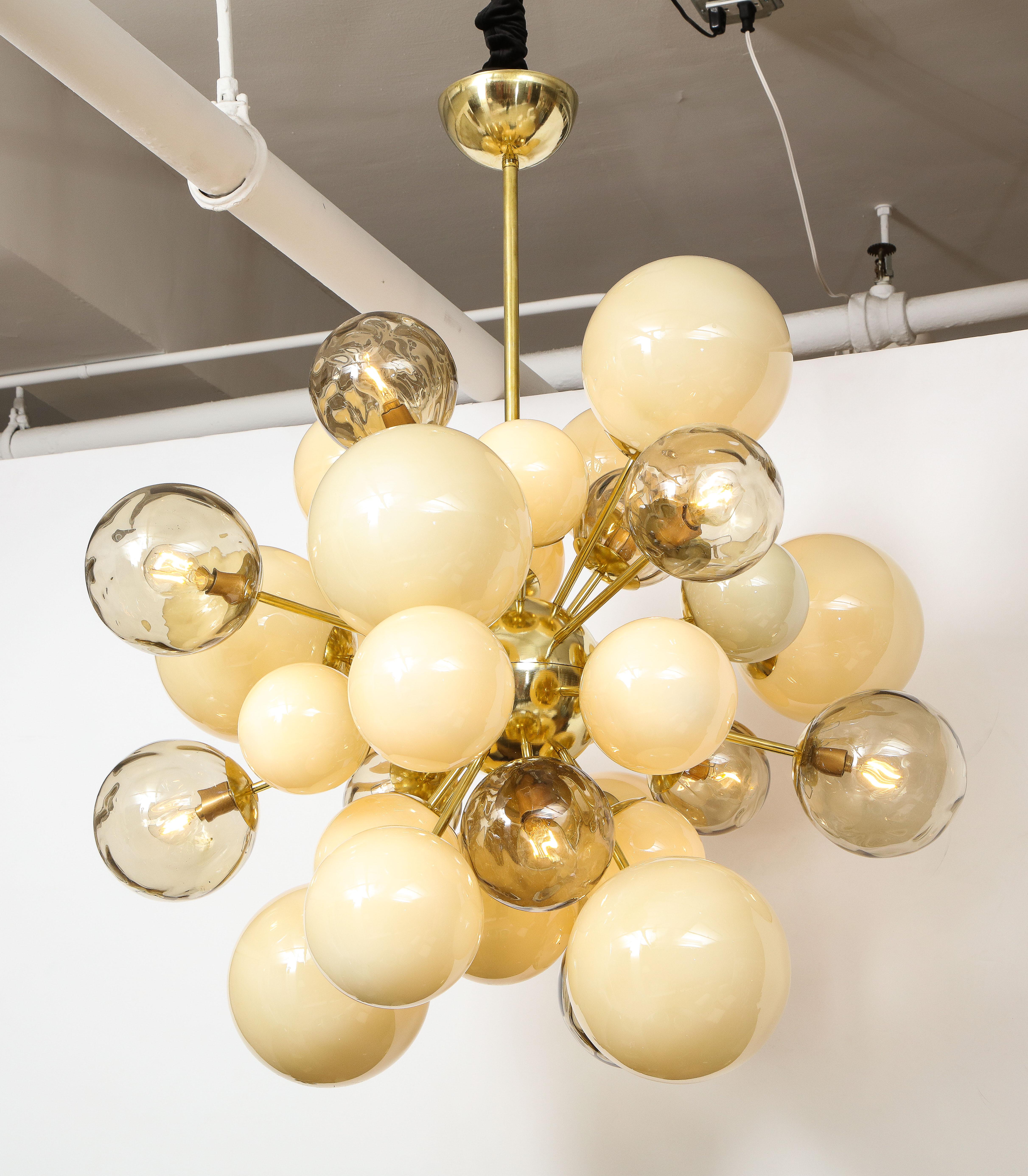 Unique sputnik or starburst chandelier consisting of hand blown, ivory and smoked taupe murano glass globes or spheres of various sizes in both clear and opaque glass finish. Each glass globe is connected to a brass rod which radiates from a brass