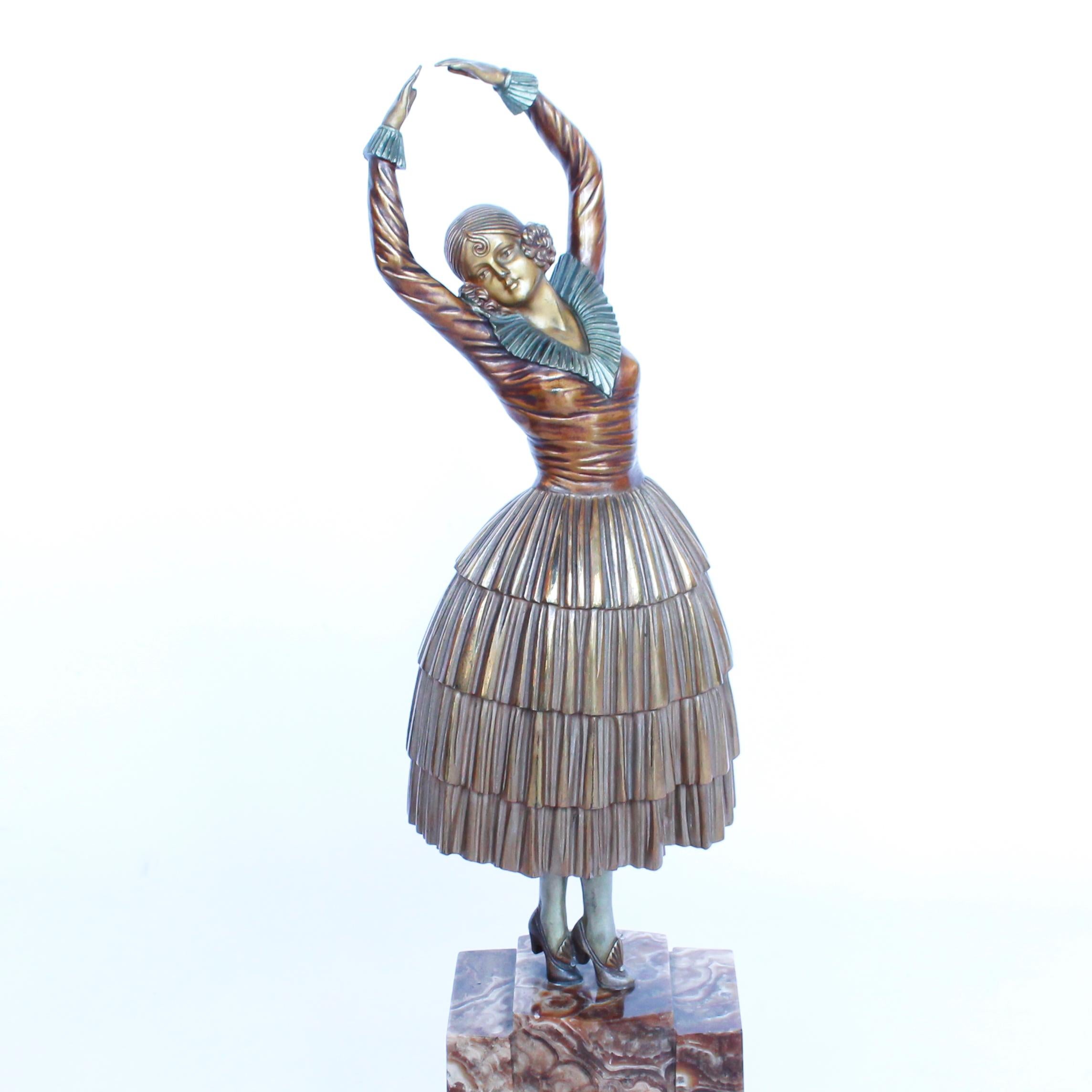 An Art Deco, cold painted gilt and enamel bronze figurine of a dancer wearing period attire, dancing on a brown, onyx stepping plinth. Signed 