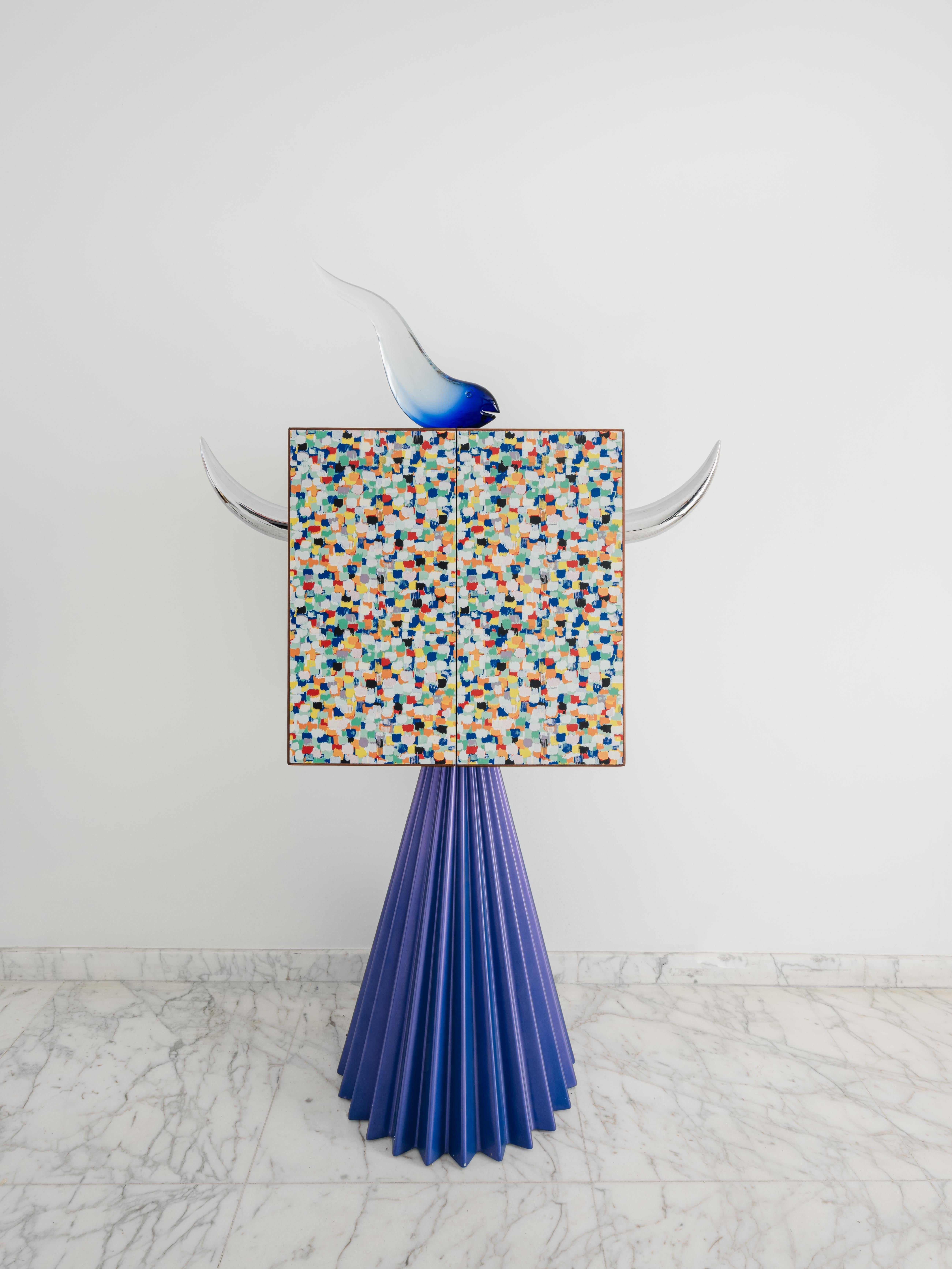 El armario Cléone Spinoza, diseñado en 1993 por Alessandro Mendini, refleja su visión del diseño como lenguaje narrativo y filosófico.
Figura destacada del postmodernismo y teórico del movimiento Alchimia, Mendini difumina la frontera entre función