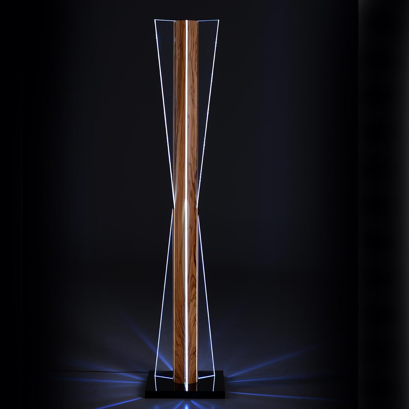 This elegant floor lamp evokes the silhouette of an hourglass, the ancient symbol for time, combined with an olive wood structure, which represents nourishment, tradition and life. Its design is both modern and classic, for a unique elegance and