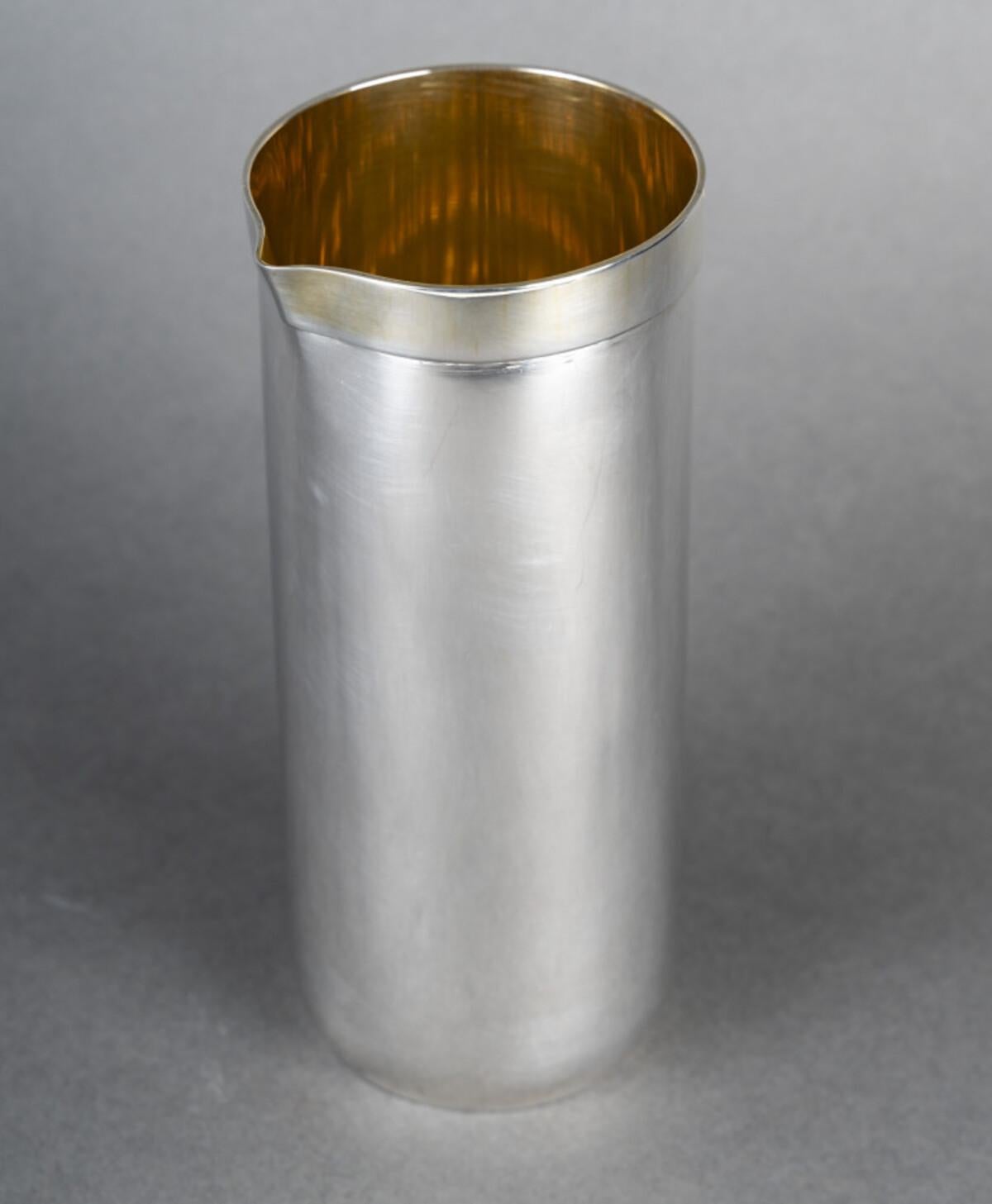 Jarra de plata maciza con interior de vermeil, en forma de tubo, el cuello está dobladillado con una banda plana y tiene un pitorro, el cuerpo está ligeramente inclinado hacia este pitorro.

Dimensiones: altura 20,5 CM - diámetro del cuello 9,5 CM -