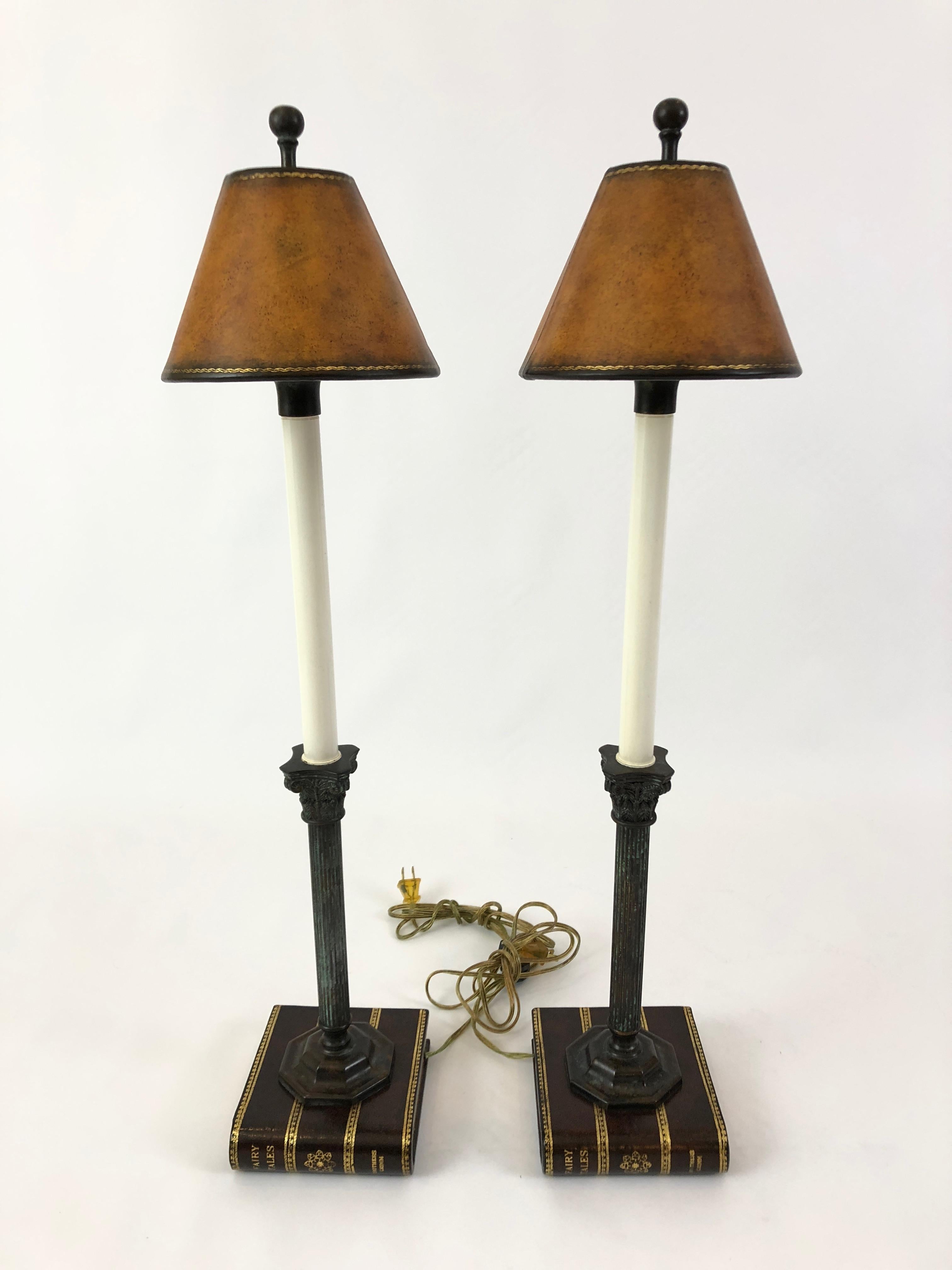 A clever pair of table lamps having bases that look like fancy leather and gold leaf books, with handsome carved wood neoclassical column candlesticks topped with leather shades.
