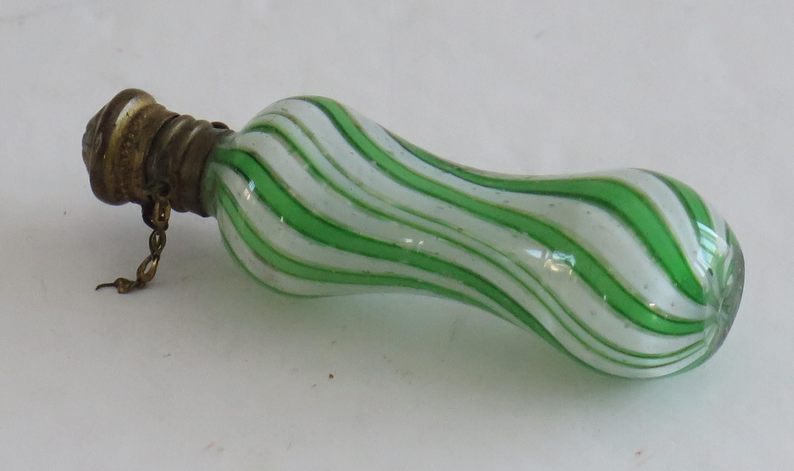 This is an antique spiral glass perfume or scent bottle, that we attribute to Clichy, France, made circa 1850.

The bottle is hand made of a green and white latticino swirling or spiral stripes (canes) in cased clear glass with a waisted form. It