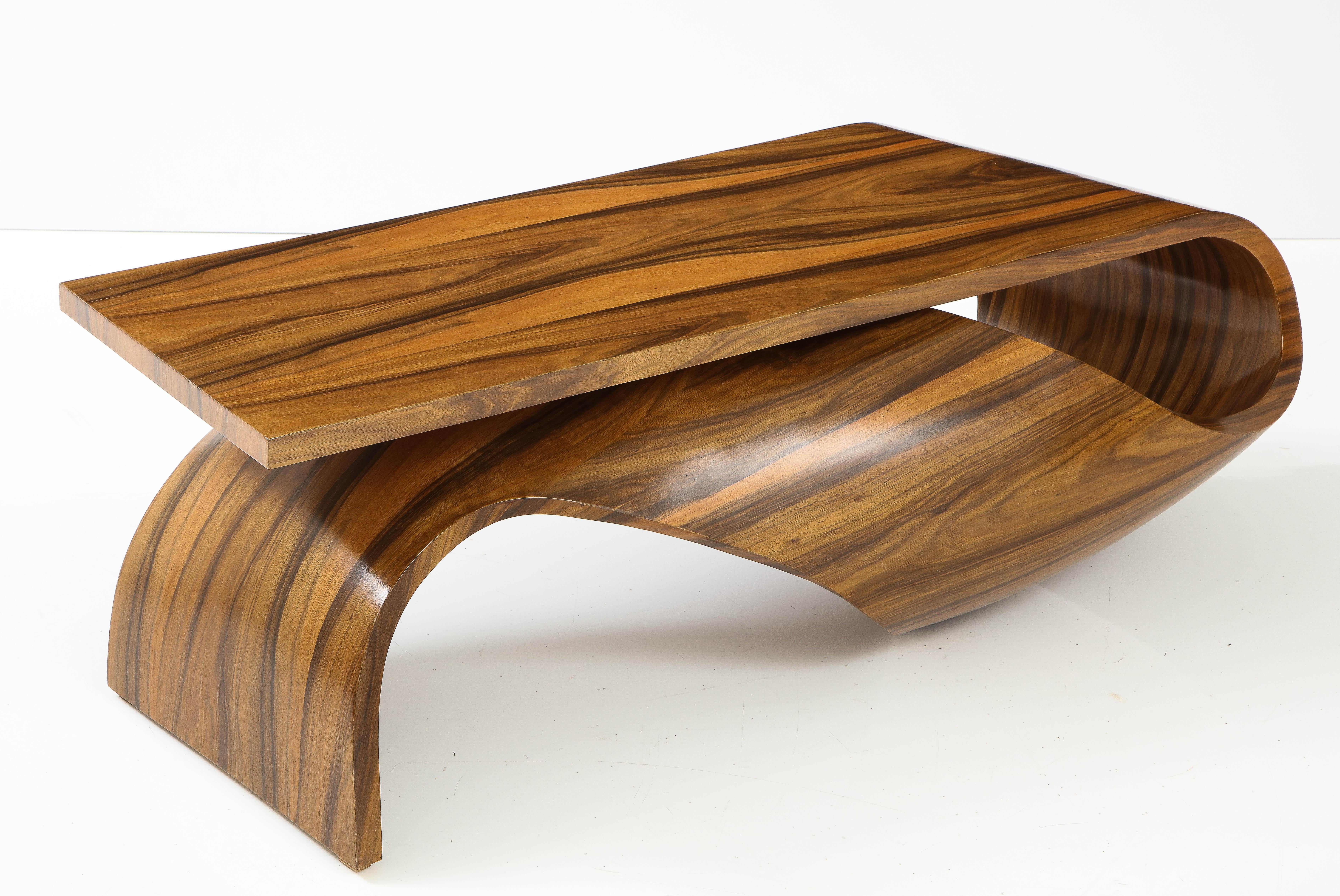 A vintage bentwood coffee table in a single piece of exotic zebra wood with elegant ribbon-like curves and undulating surfaces with a rectangular top resting on one curved side and a triangular ebonized leg on the other. This cocktail table is a
