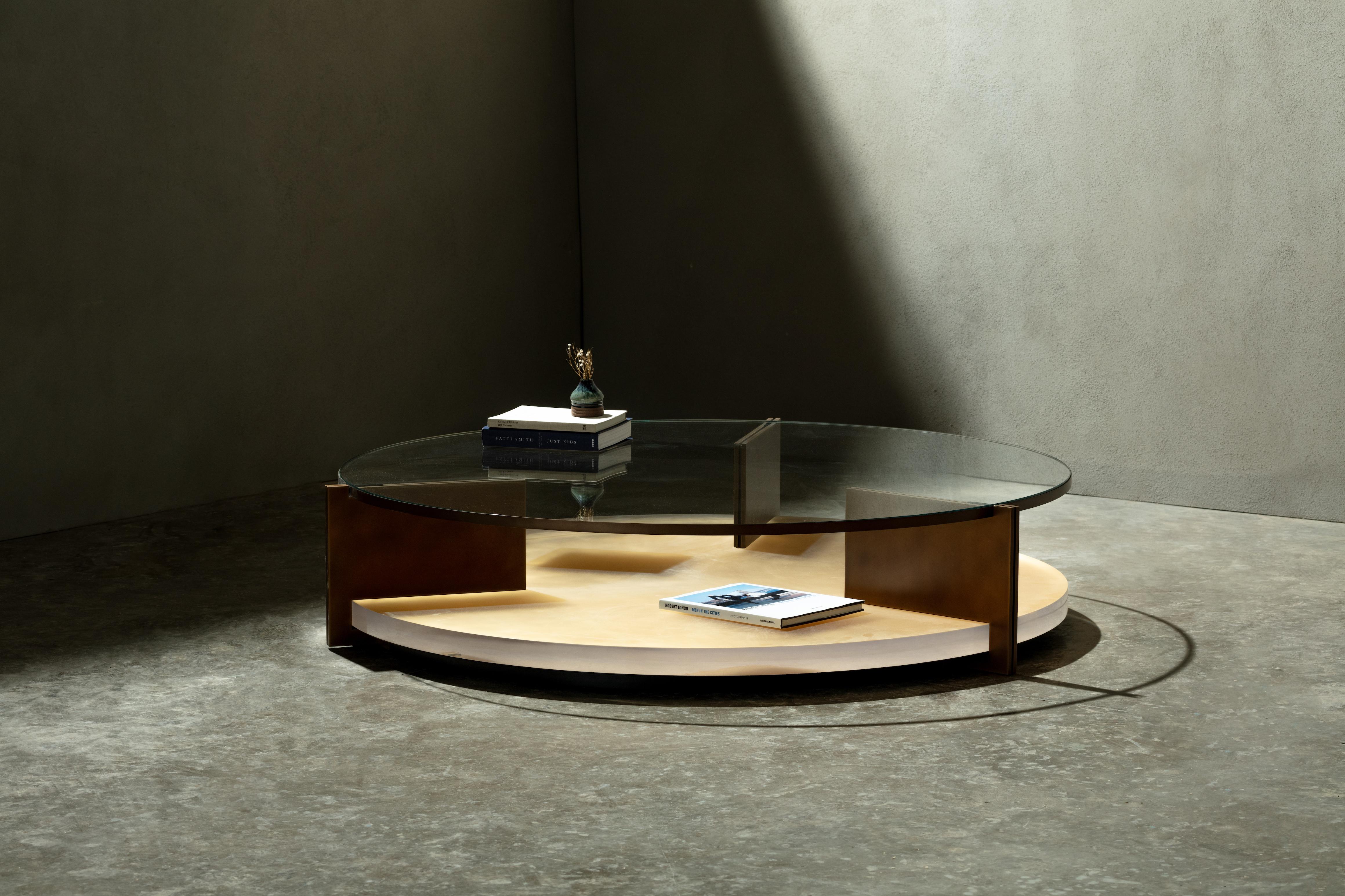 Inspired by the Umbra side table, the Clio coffee table boasts an extra clear glass top resting on a sandblasted acrylic base with silver or gold leaf backing and supported by three metal legs. The acrylic's thickness and sandblasted effect create