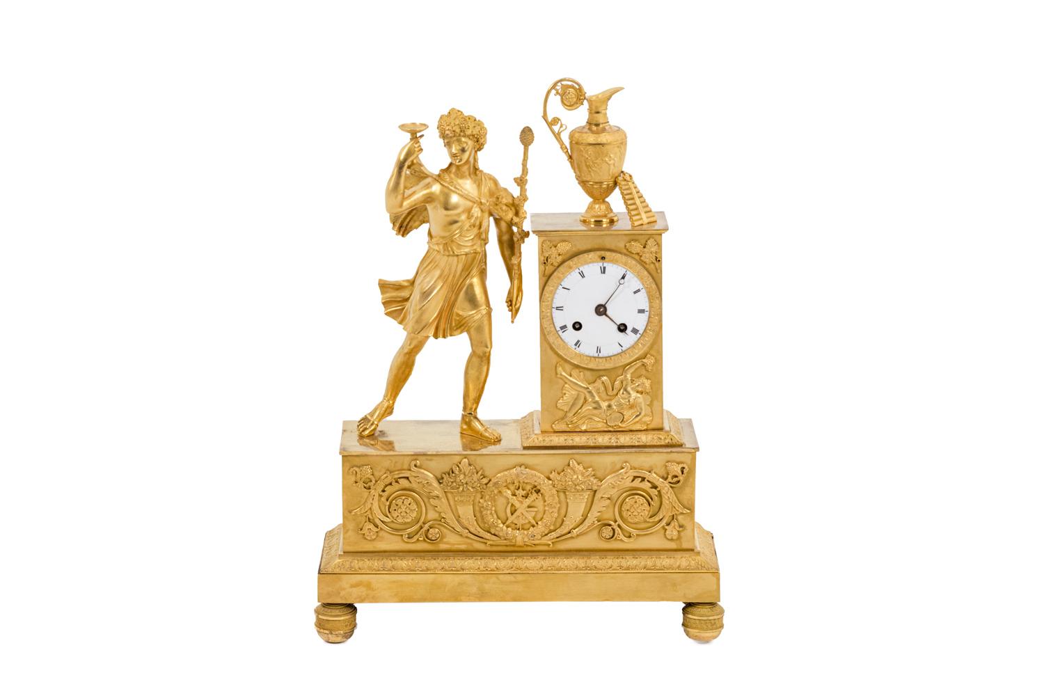 Clock in chiselled and gilt bronze composed by a rectangular base on which stand the dial-plate and a statuette of Bacchus. Round dial-plate with Roman numbers off-center on the right part. Façade adorned with horns of abundance, vegetal scrolls,