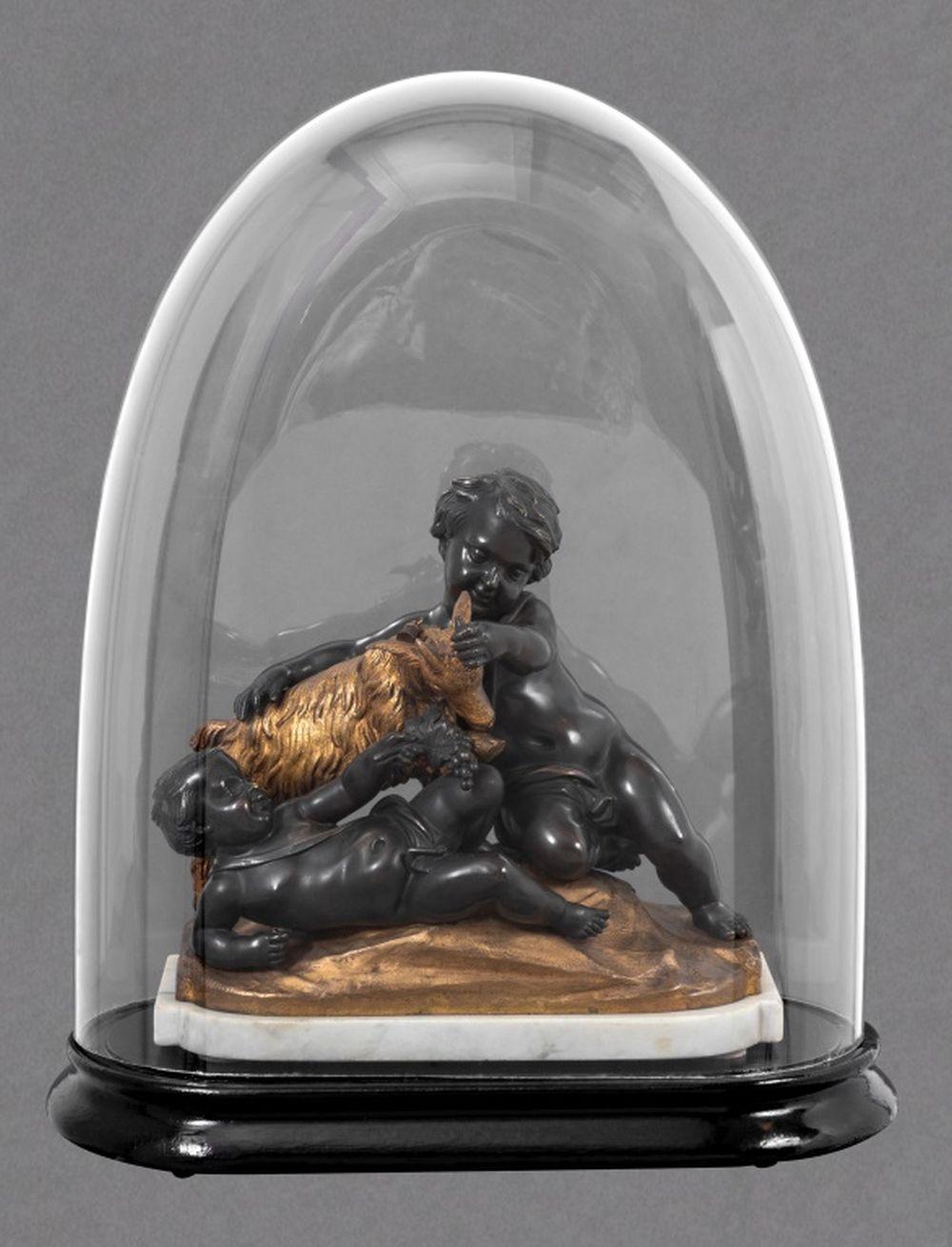 After Clodion (Claude Michel, French, 1738-1814) Figural Group Patinated and Gilt Bronze Sculpture, 19th century, depicting two cherubs playing with a goat, on a white marble base, under a glass dome and ebonized stand. Bronze: 10.25
