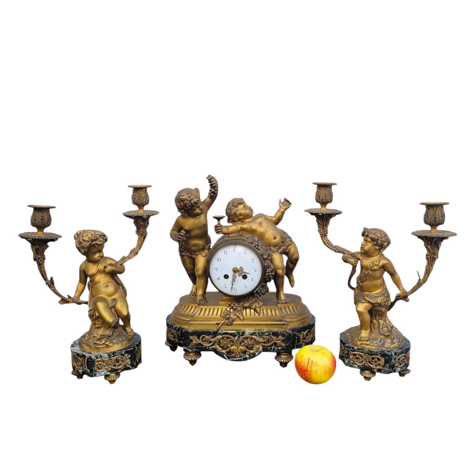 Gilt bronze mantelpiece set, composed of a clock and two candelabras, on a green marble base 

 This set presents the theme of bacchanalia and autumn, loves celebrate the vine and wine: rich decoration of grapes, vine leaves and cups 

We find