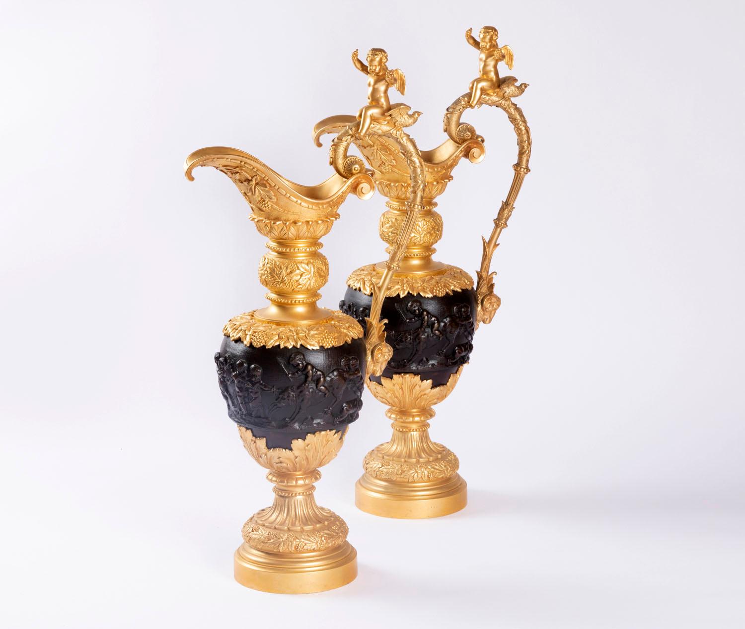 After Clodion.

Pair of bronze ewers with two patinas representing bacchanalia scenes after Clodion. Circular base with gadroon piedouche decorated with beads and vine leaves friezes. Gilt bronze mount with large stylized acanthus leaves. Brown