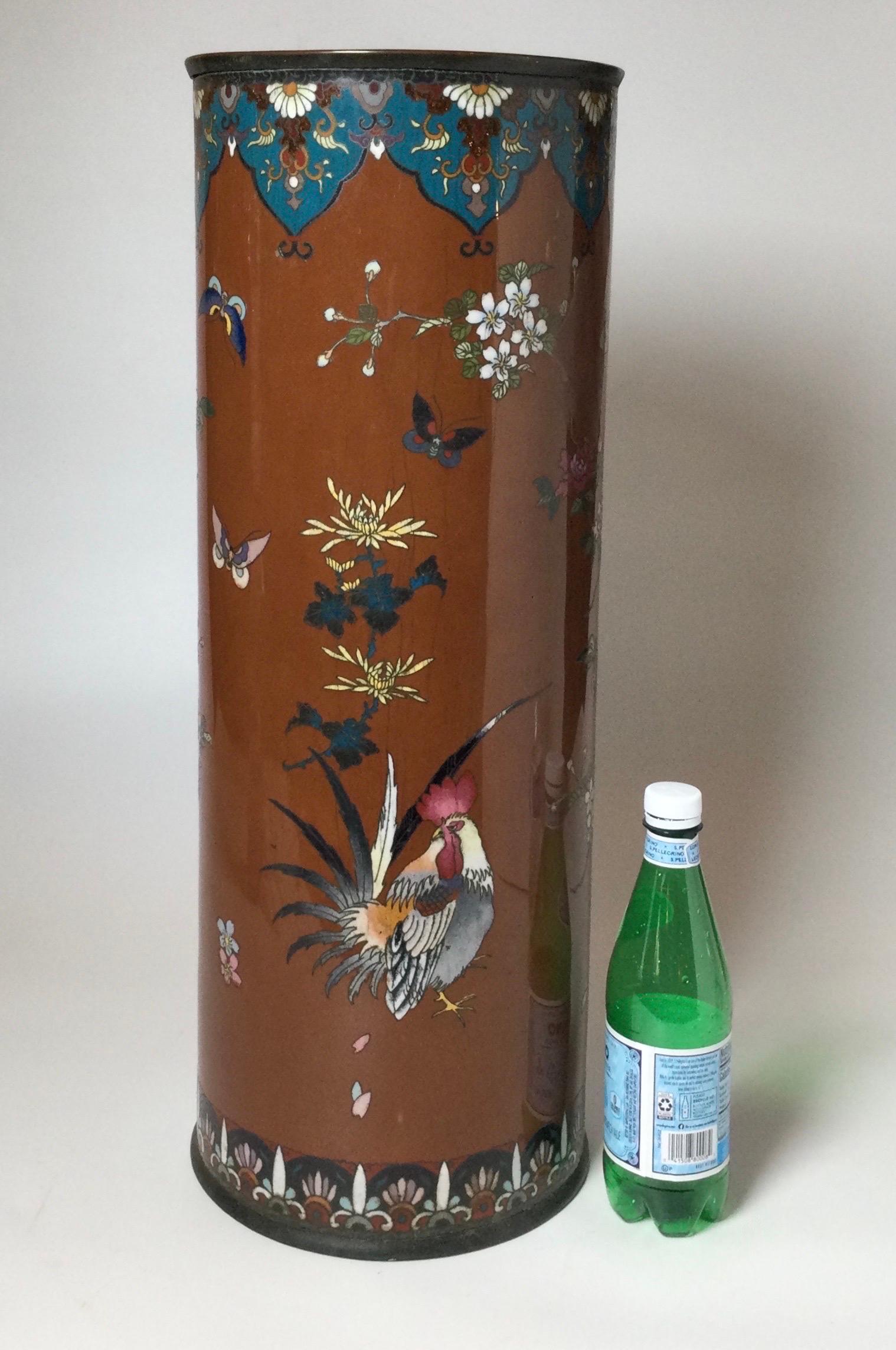 A cylindrical cloisonné can or umbrella holder with multicolor floral bird and butterfly decoration. useful item, beautifully designed. The are some age related stress cracks as shown in pictures with on small repair to the brown background.
