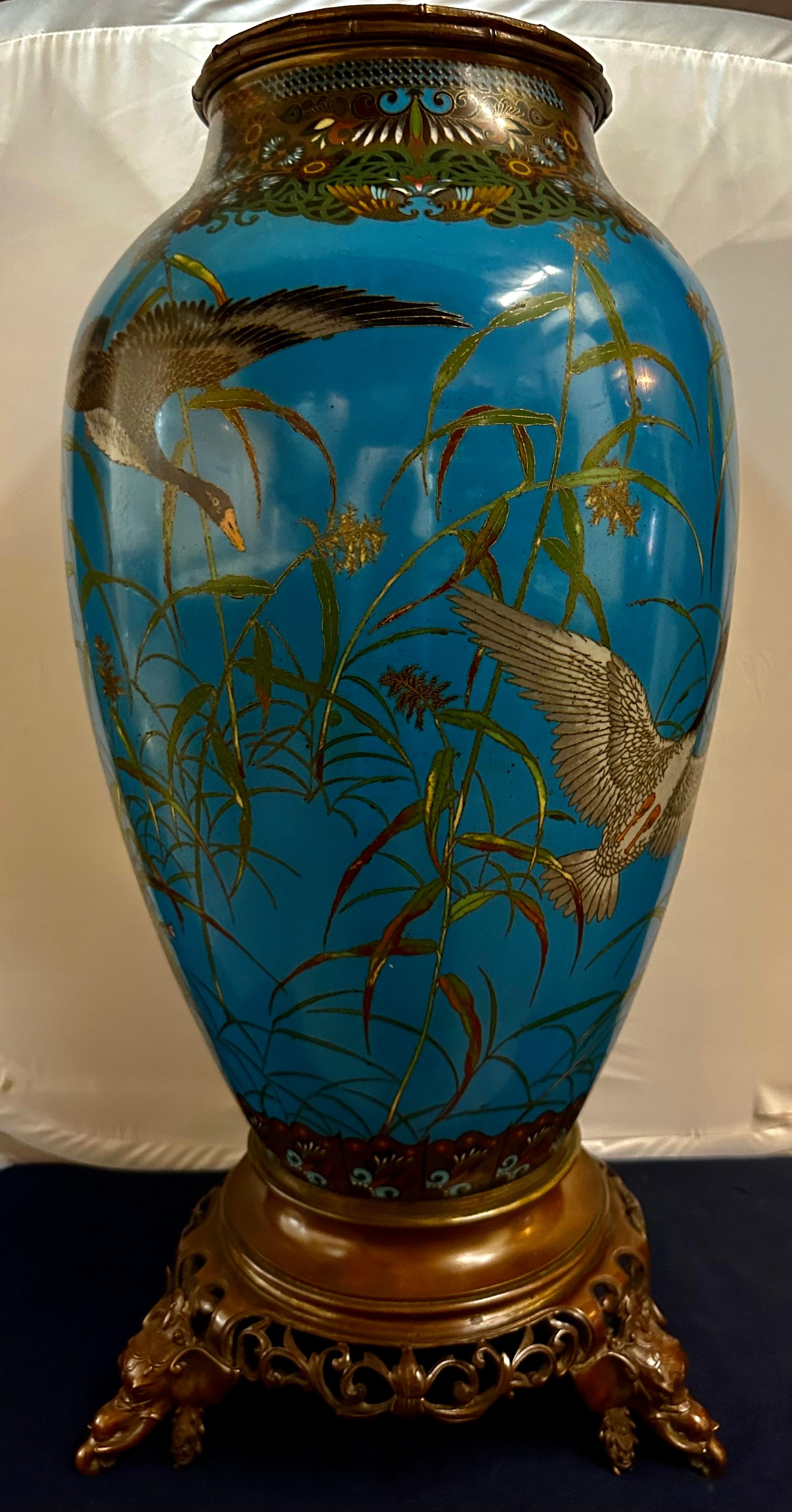 This magnificent vintage Japanese cloisonné floor vase dates from the late 19th century. It is hand enameled & artistically rendered with multiple wild geese in flight. The geese are seen rising from the Japanese pampas grass against a deep blue